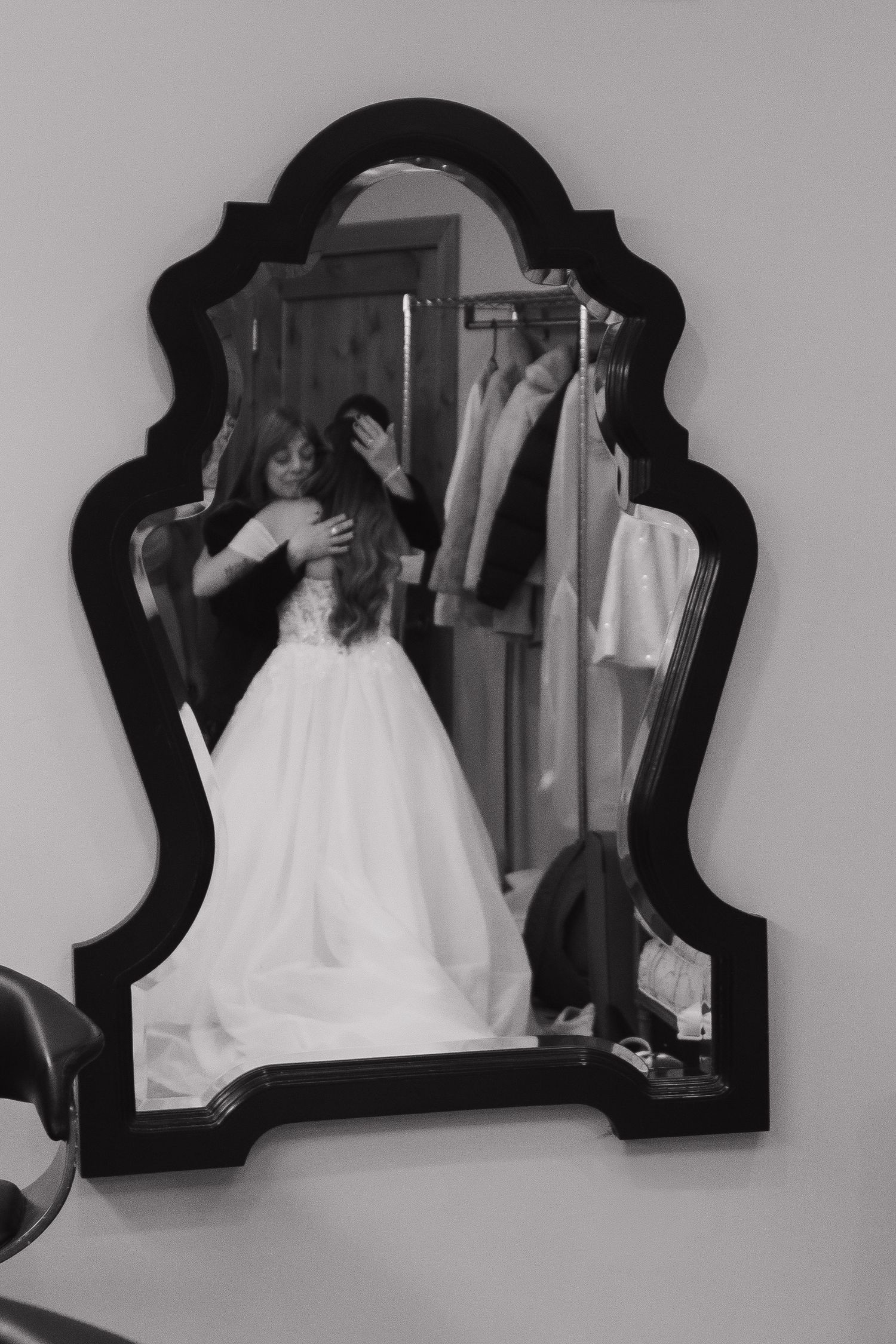 A wedding dress reflection in an ornate black-framed mirror during preparation.