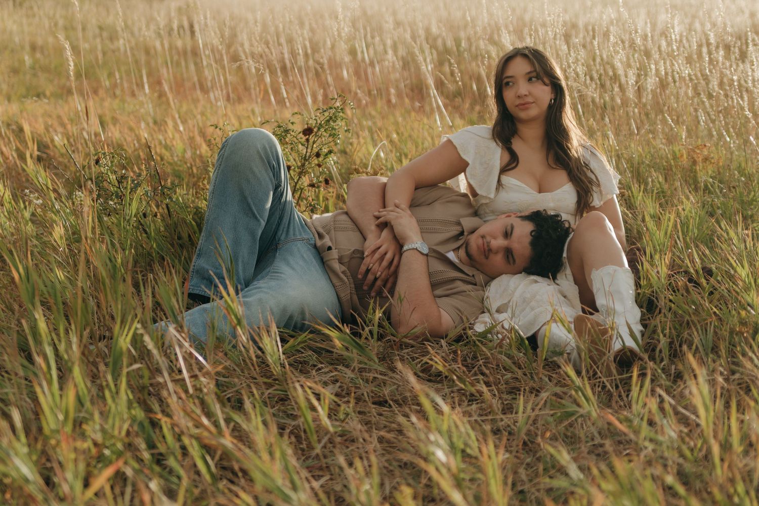 Couple lying in golden grass field, woman resting as man lays in her lap at sunset.