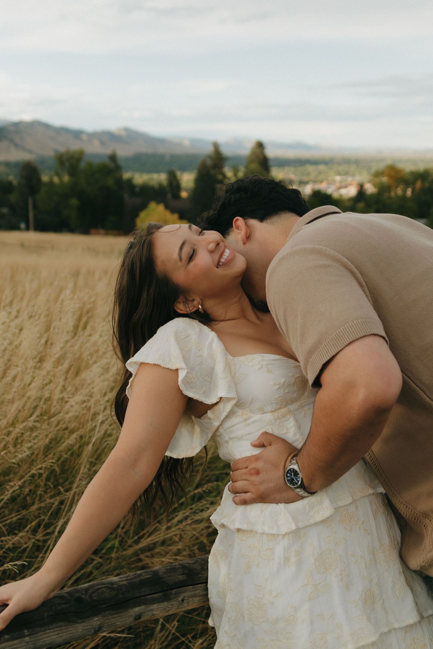 Couple shares a romantic moment by fence in golden field, woman laughing joyfully.