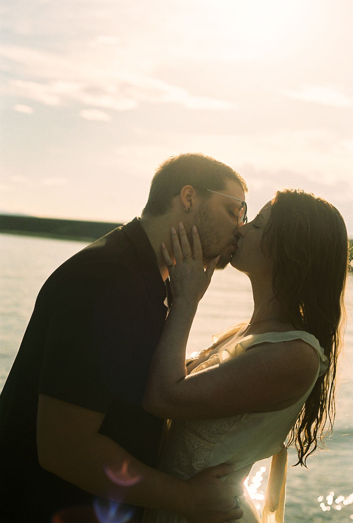 Silhouetted couple sharing a passionate kiss backlit by golden sunset over a lake.