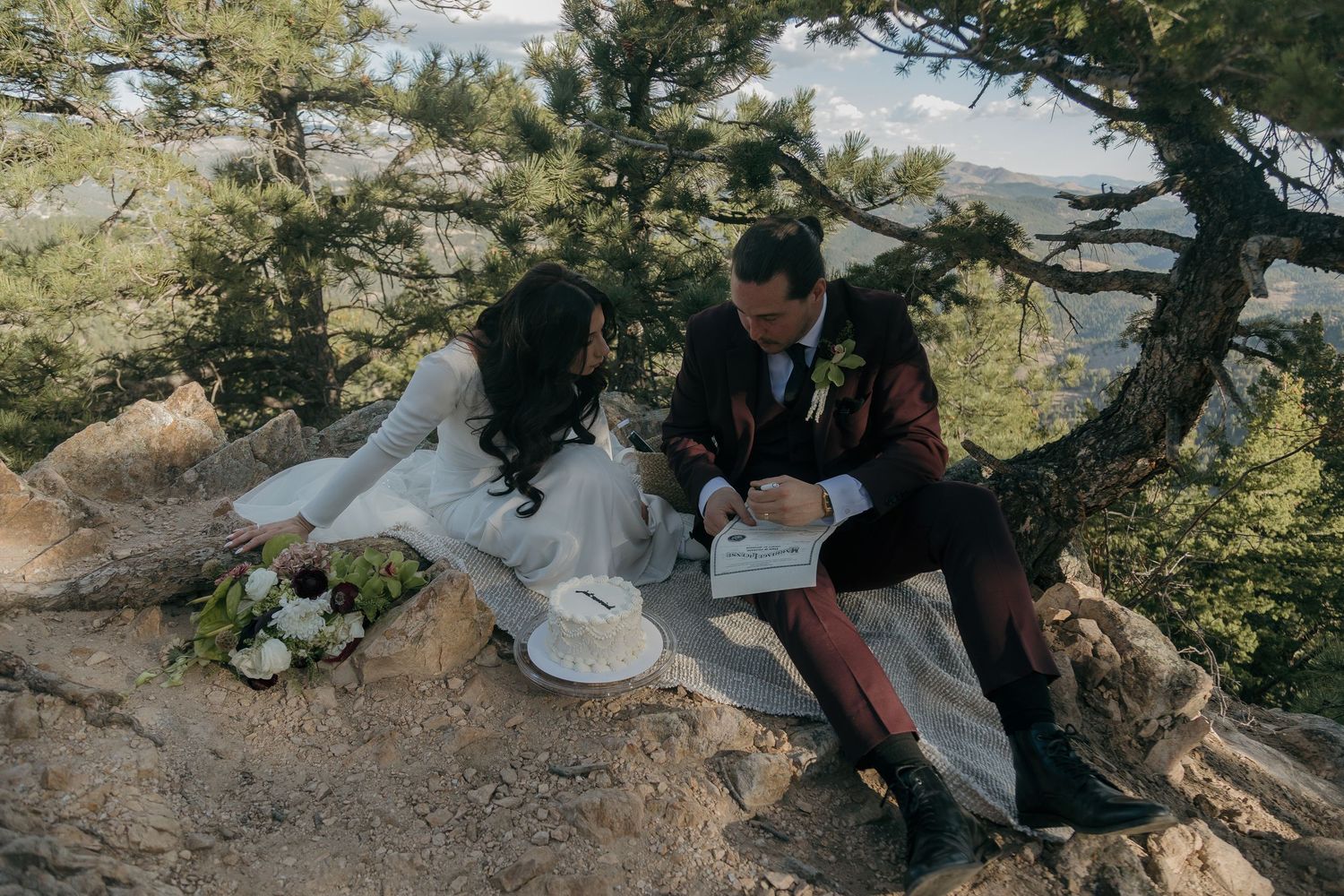 Bride and groom enjoy an intimate outdoor picnic elopement on a rocky mountain overlook with cake.
