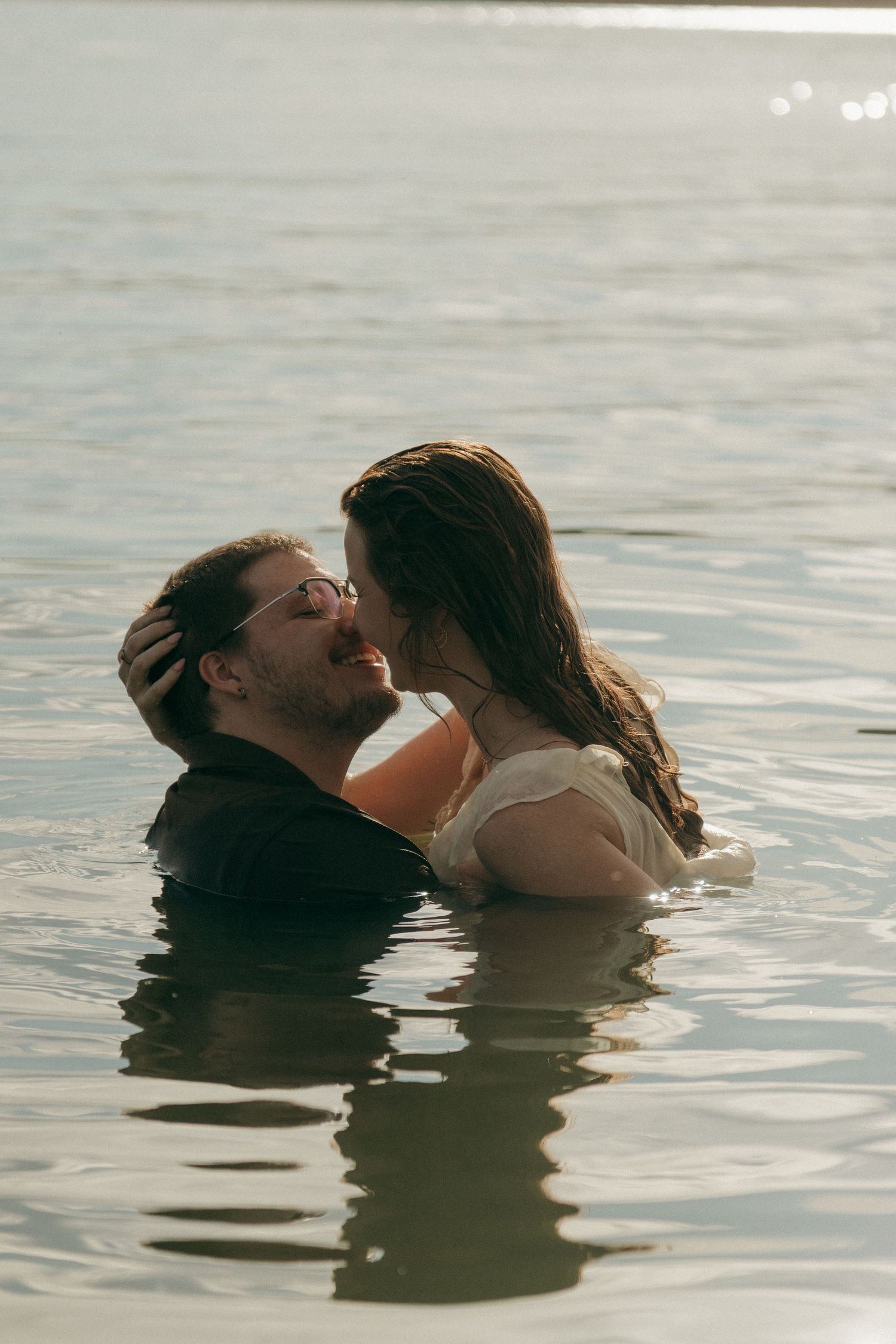 Couple sharing an intimate moment nearly submerged in a sunlit lake during a romantic photo session.