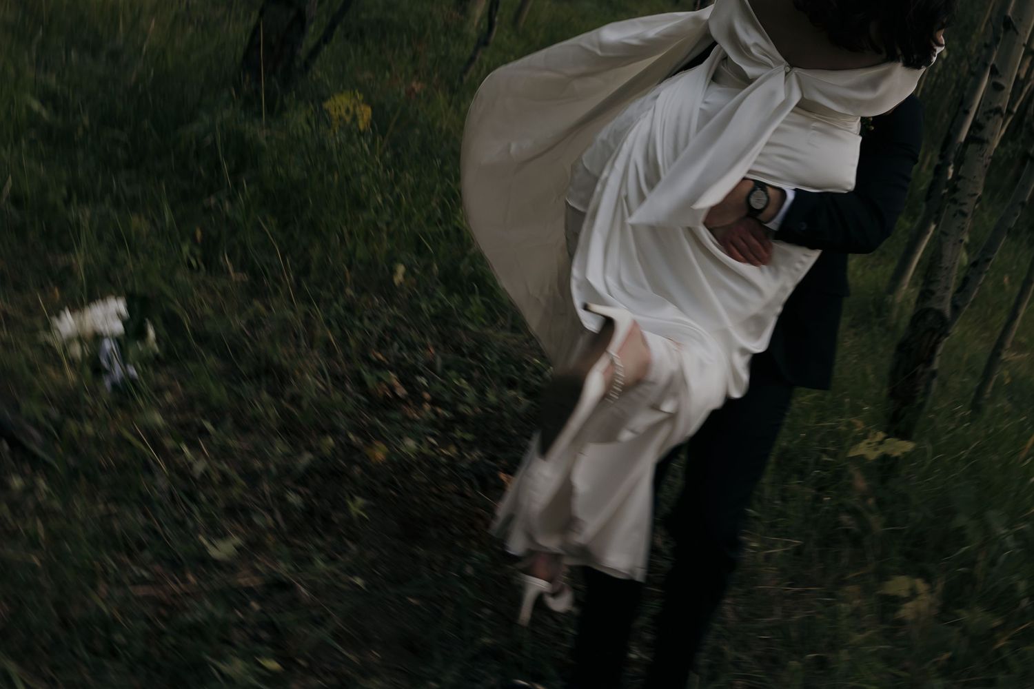 Bride in flowing white dress and groom walking through a lush green forest during wedding.
