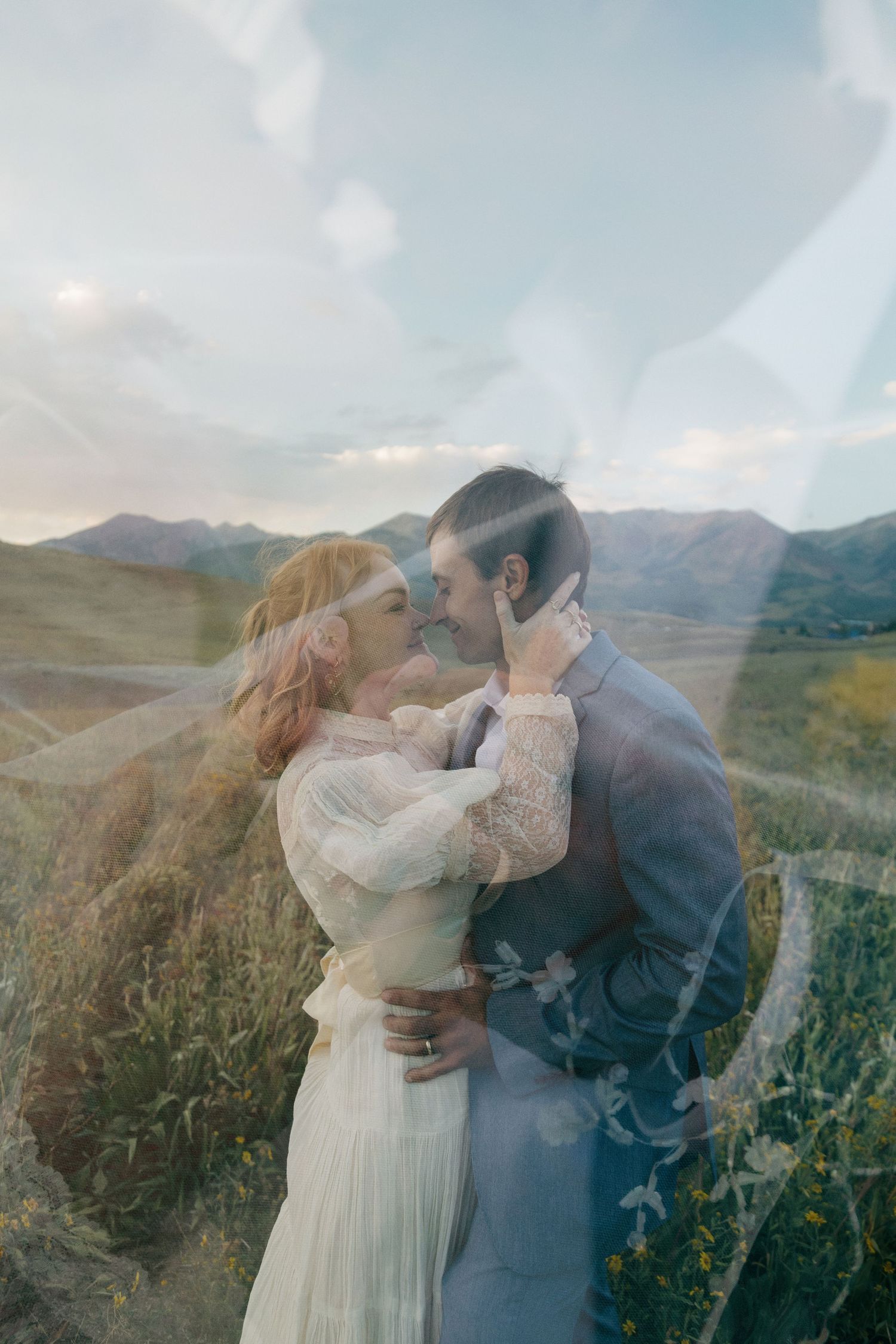 Romantic double exposure wedding photo of couple kissing with mountain landscape background.
