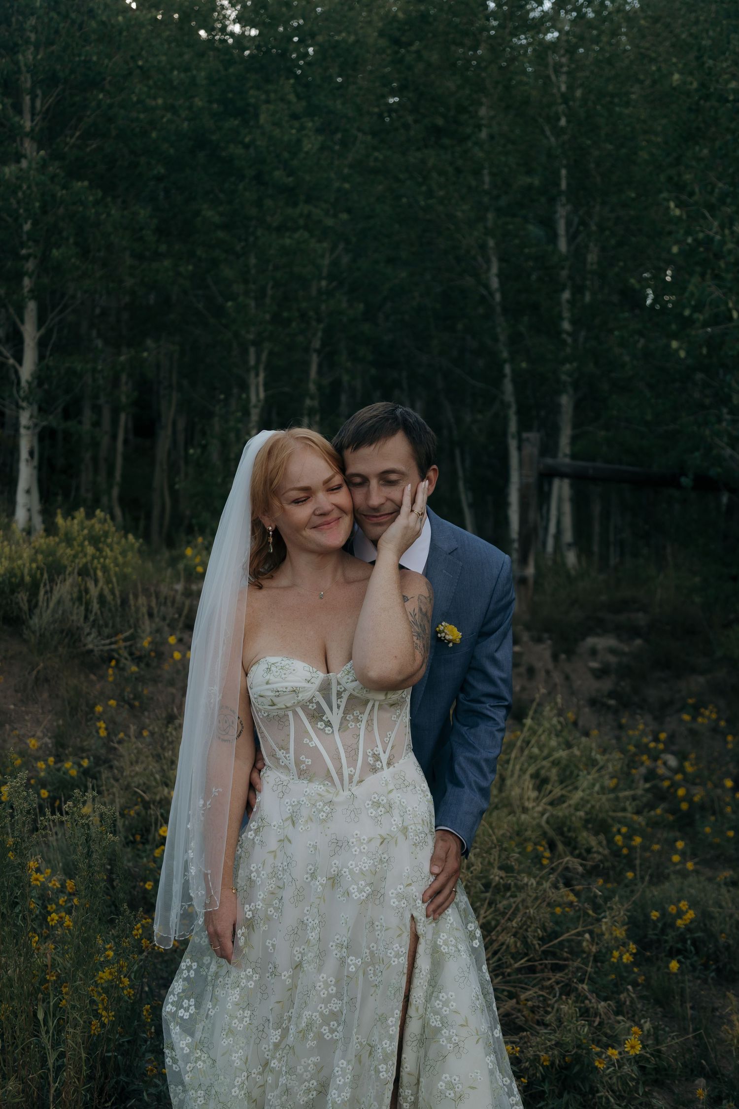 A bride and groom share a tender moment surrounded by aspen trees at dusk.