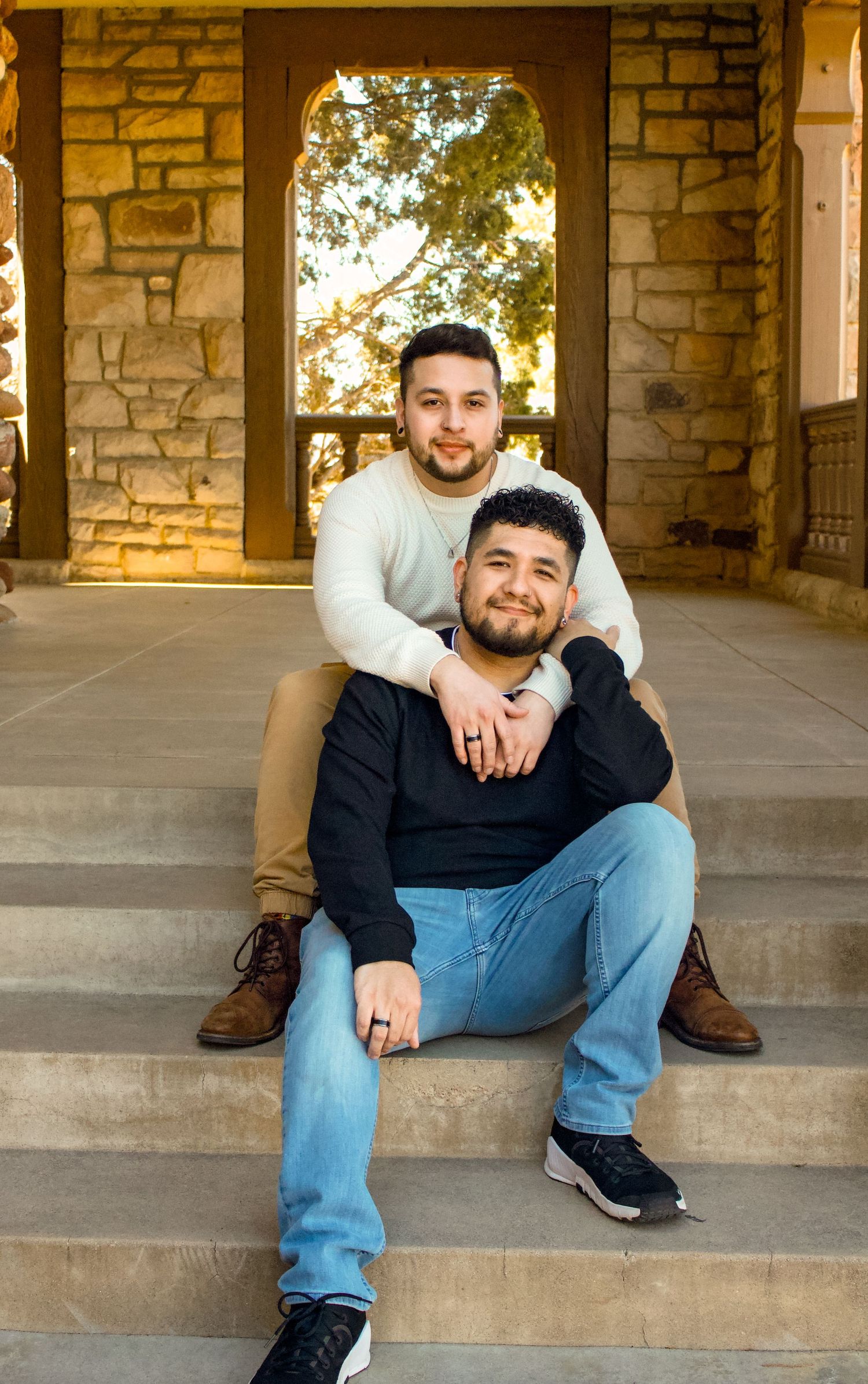 Two people posing on concrete steps with stone walls and arched window in background.