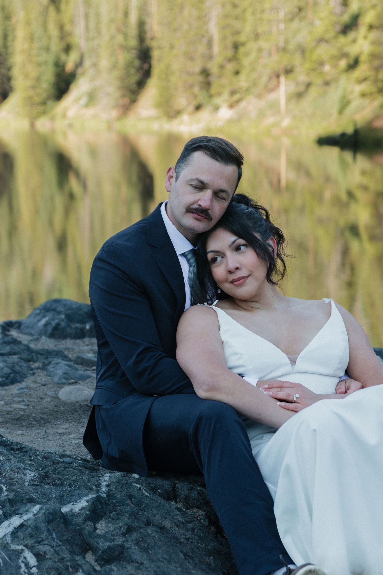 A romantic wedding photoshoot by a serene mountain lake with evergreen trees in the background.