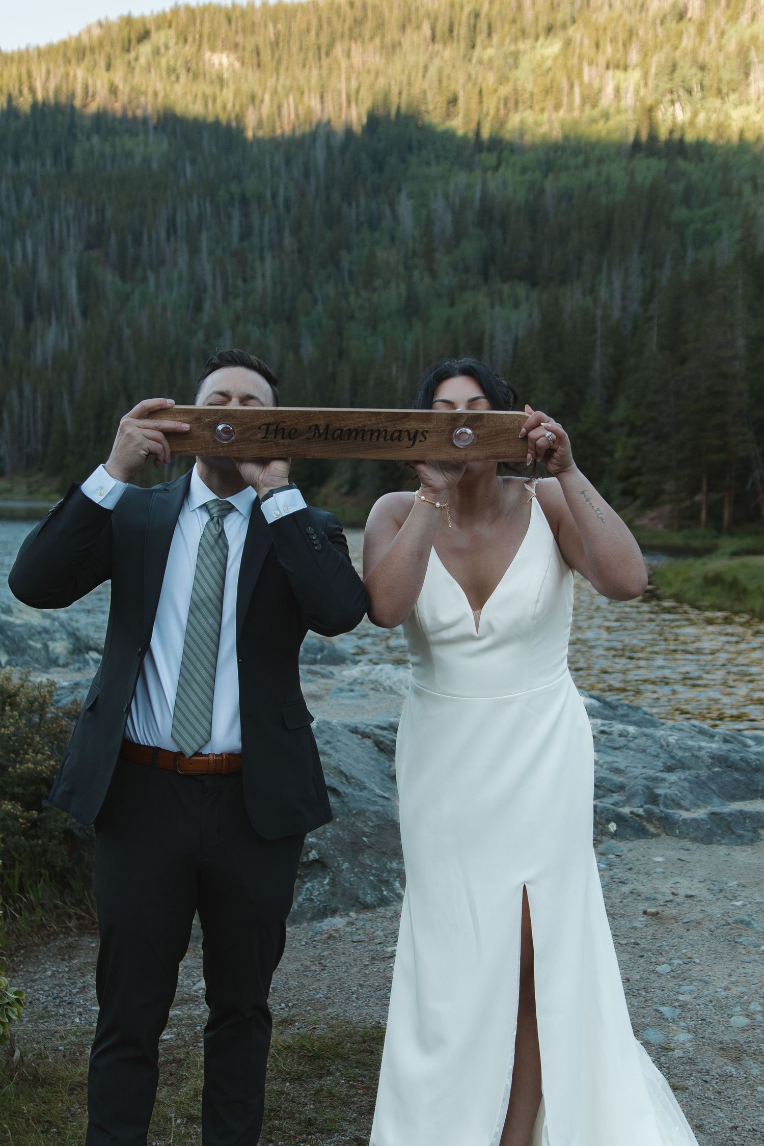 A couple poses with a wooden measuring stick against a mountain backdrop during their wedding.