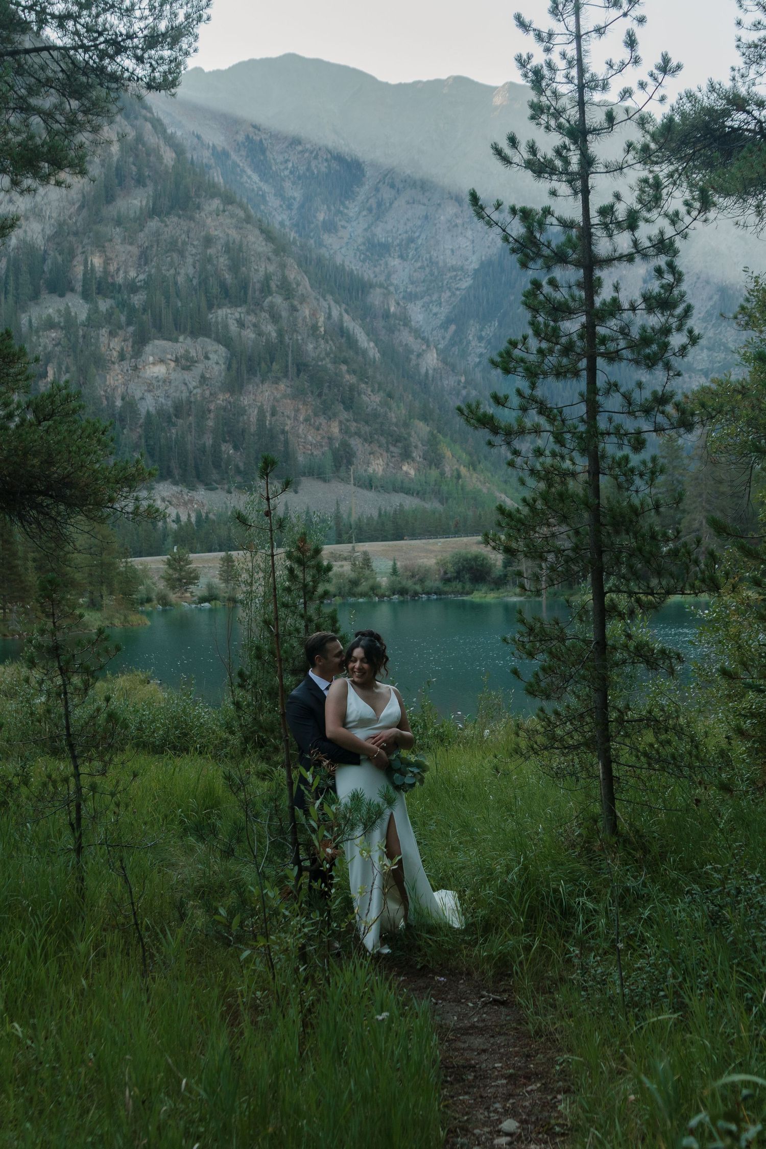 A romantic lakeside wedding scene with mountain views and evergreen trees.