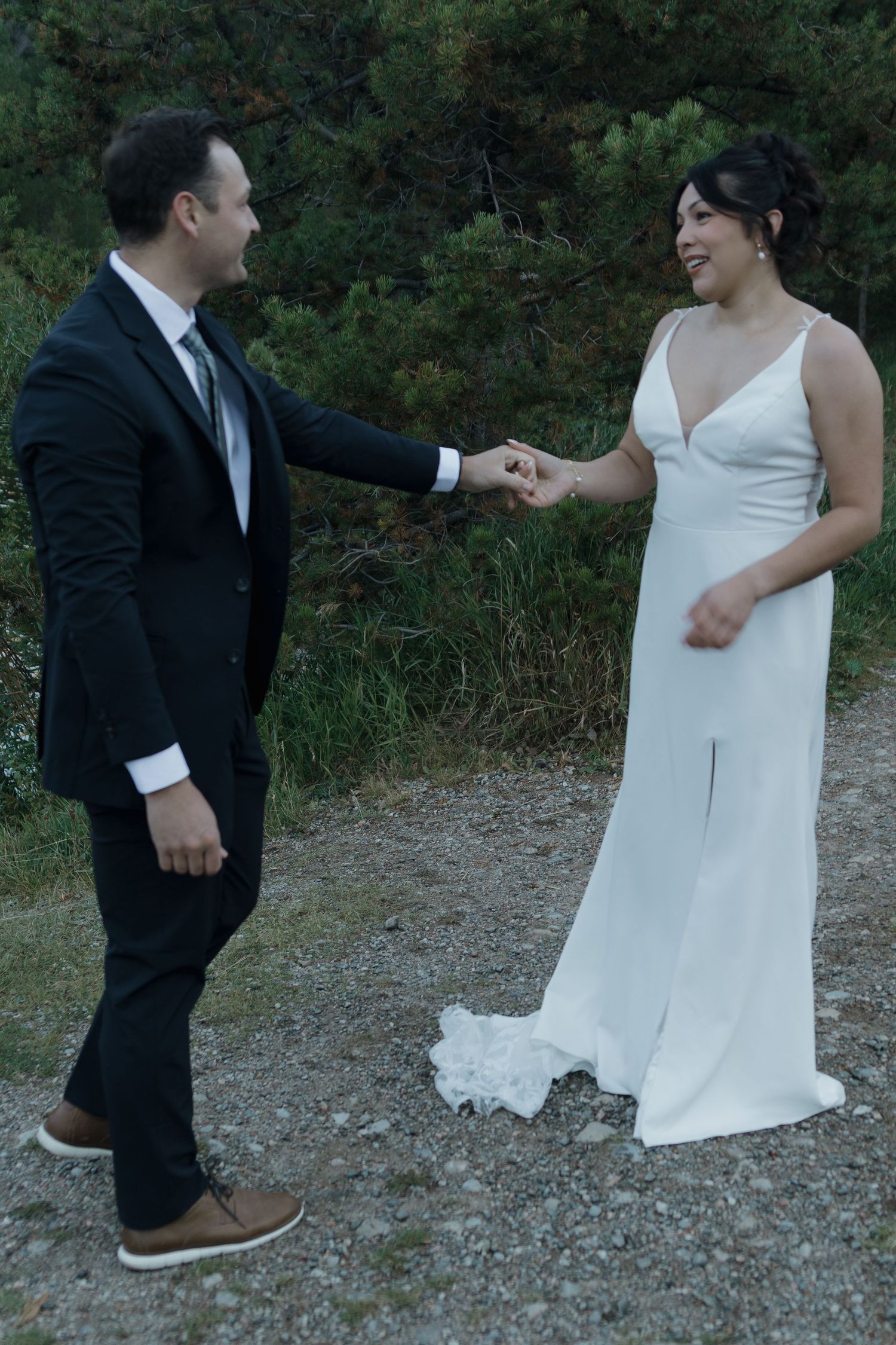 A couple in wedding attire dances together on a rocky outdoor path.