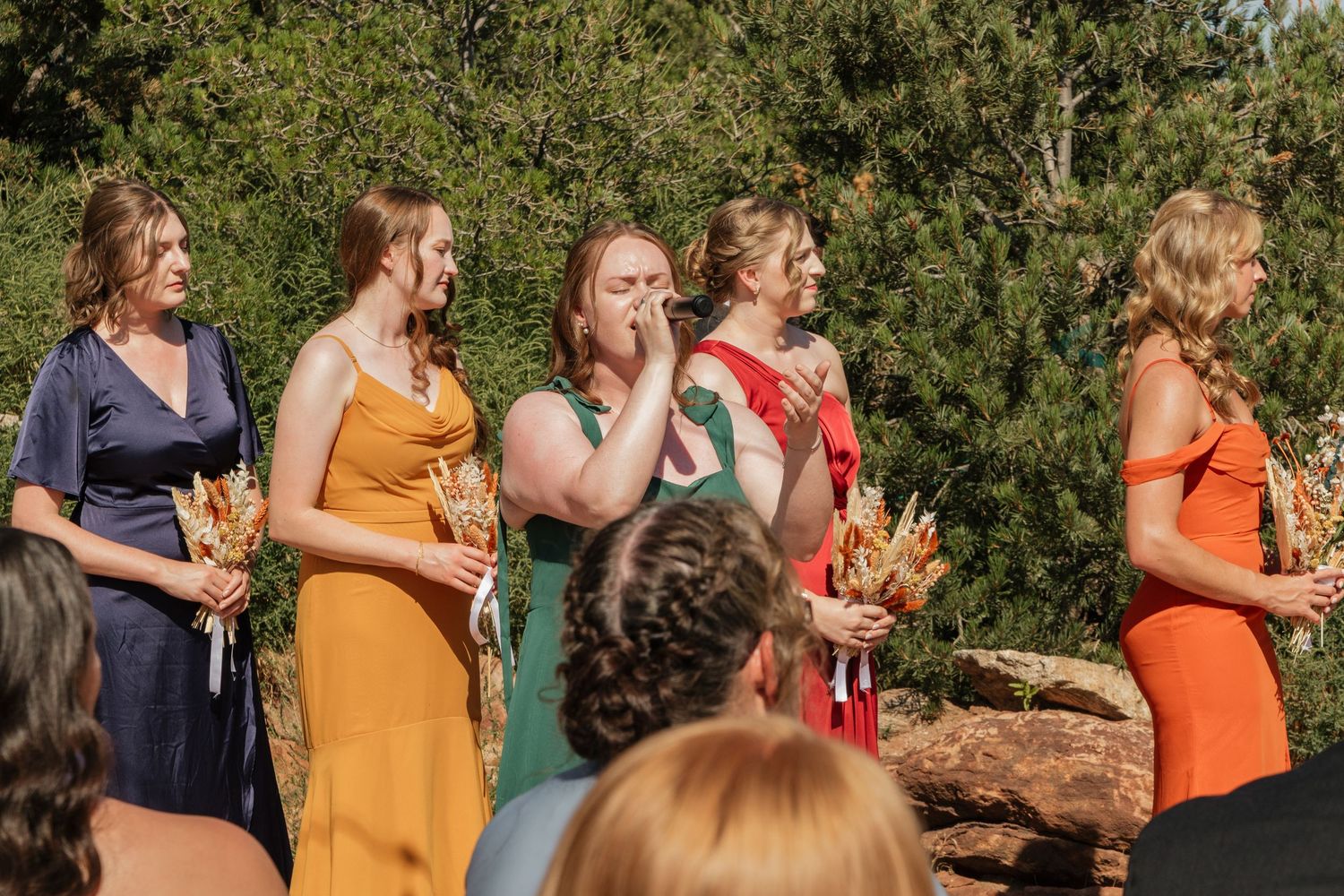 Wedding party stands in colorful dresses during an outdoor ceremony.