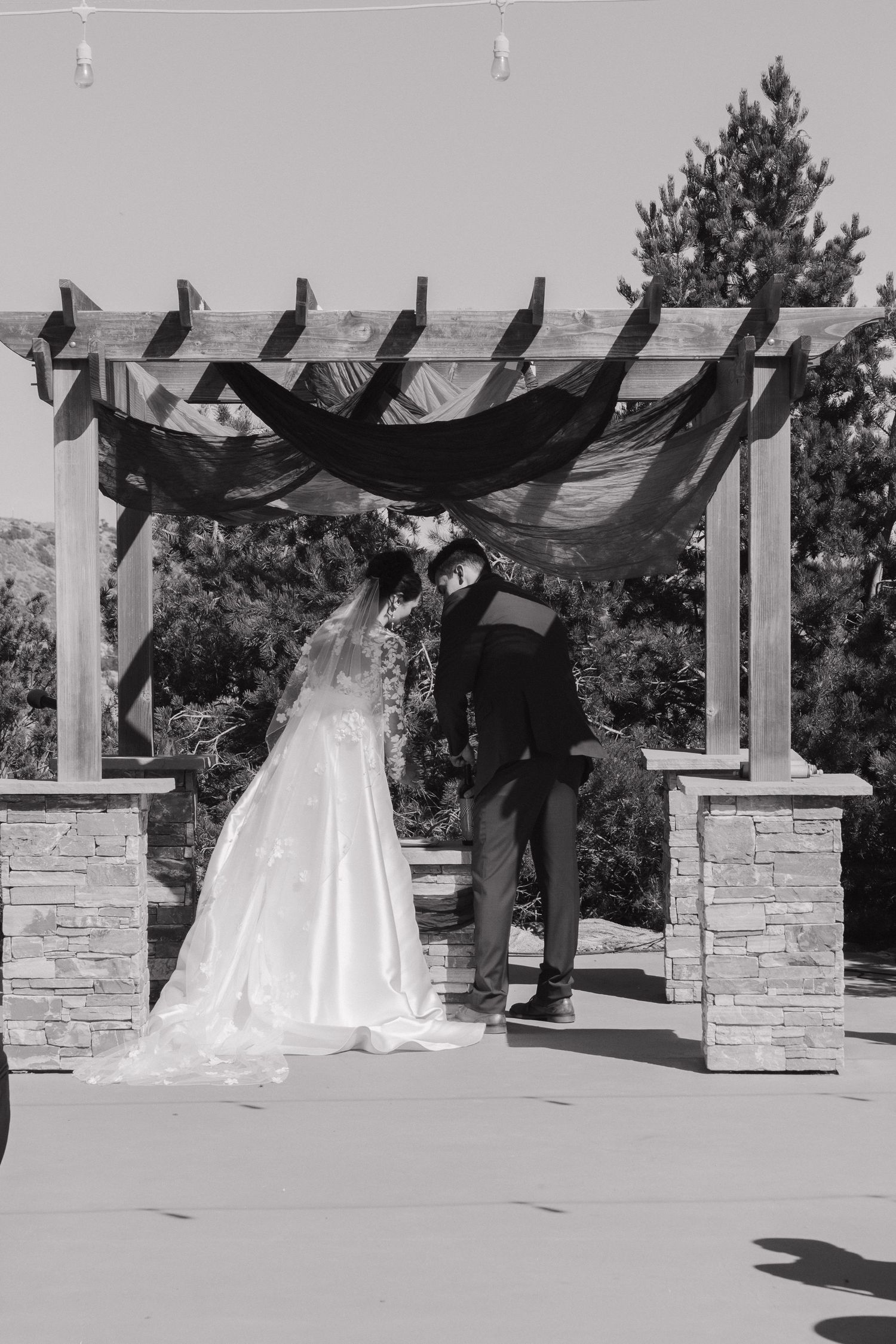 Black and white photo of a wedding ceremony under a pergola with stone pillars.