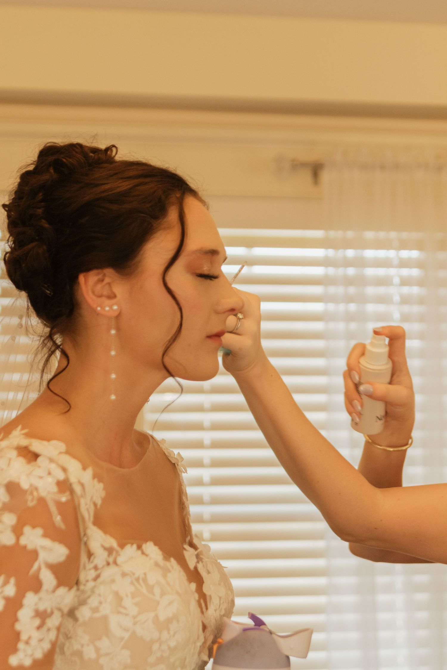 Final touches being applied to wedding day makeup in natural window light.
