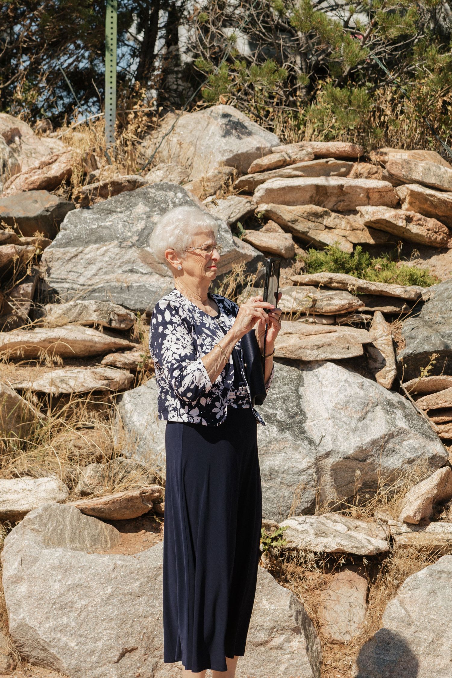 A person in a navy and floral dress poses against rocky terrain in an outdoor setting.