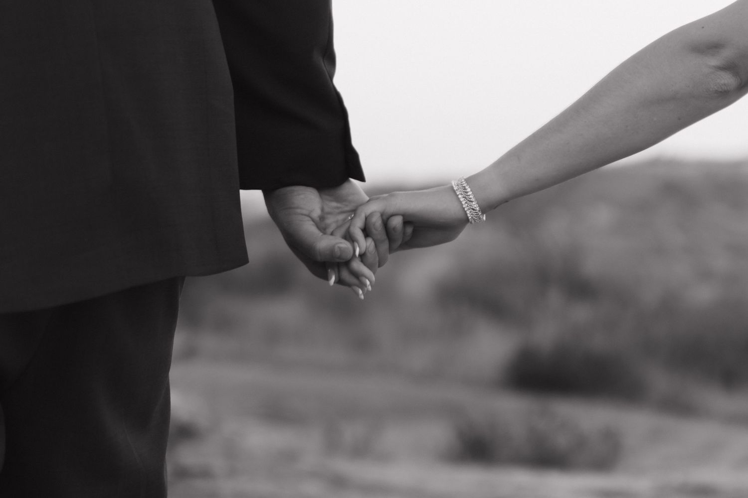 Black and white close-up of two hands clasped together in an intimate moment.