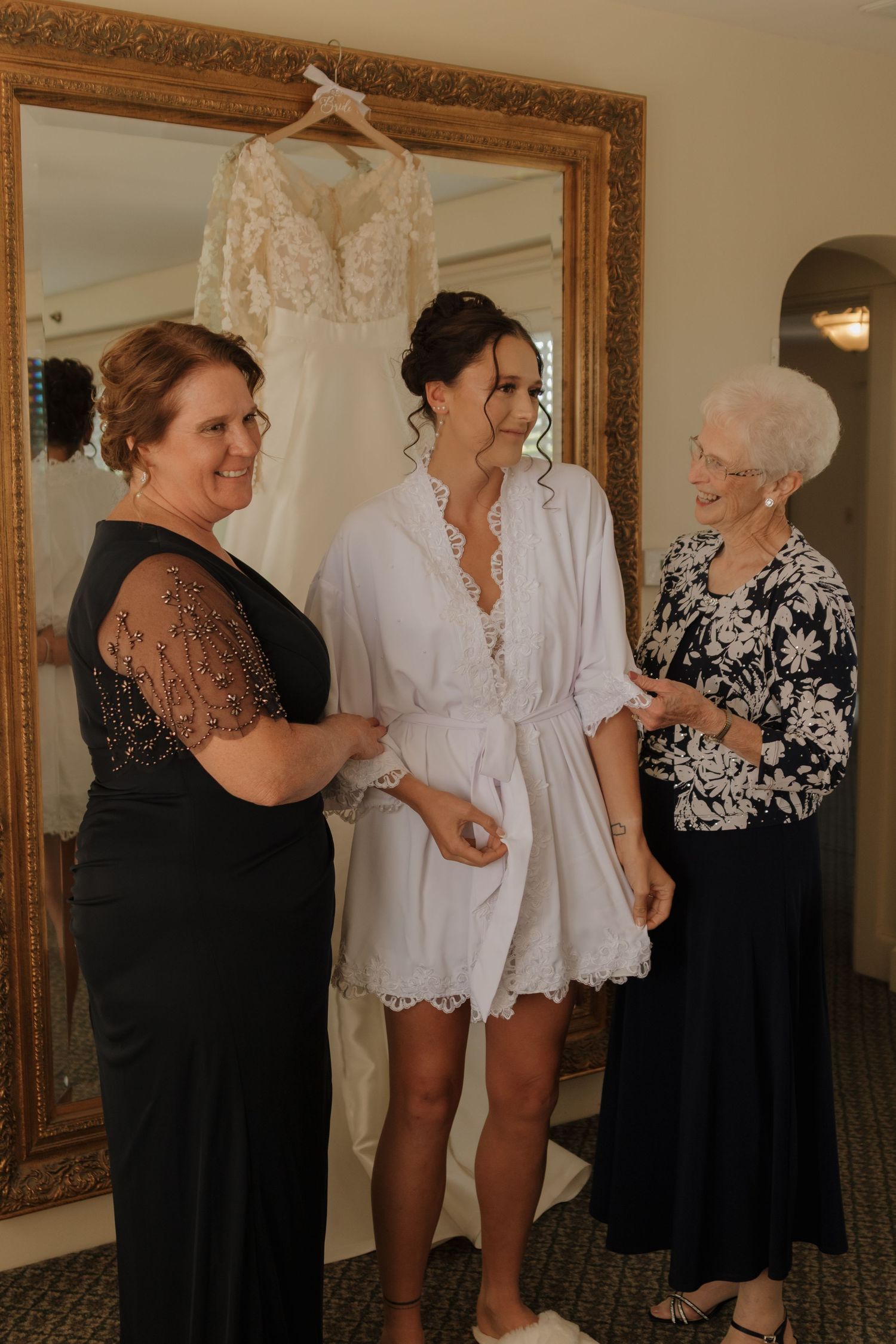 Wedding party laughing while helping with getting ready preparations in a room with ornate mirror.
