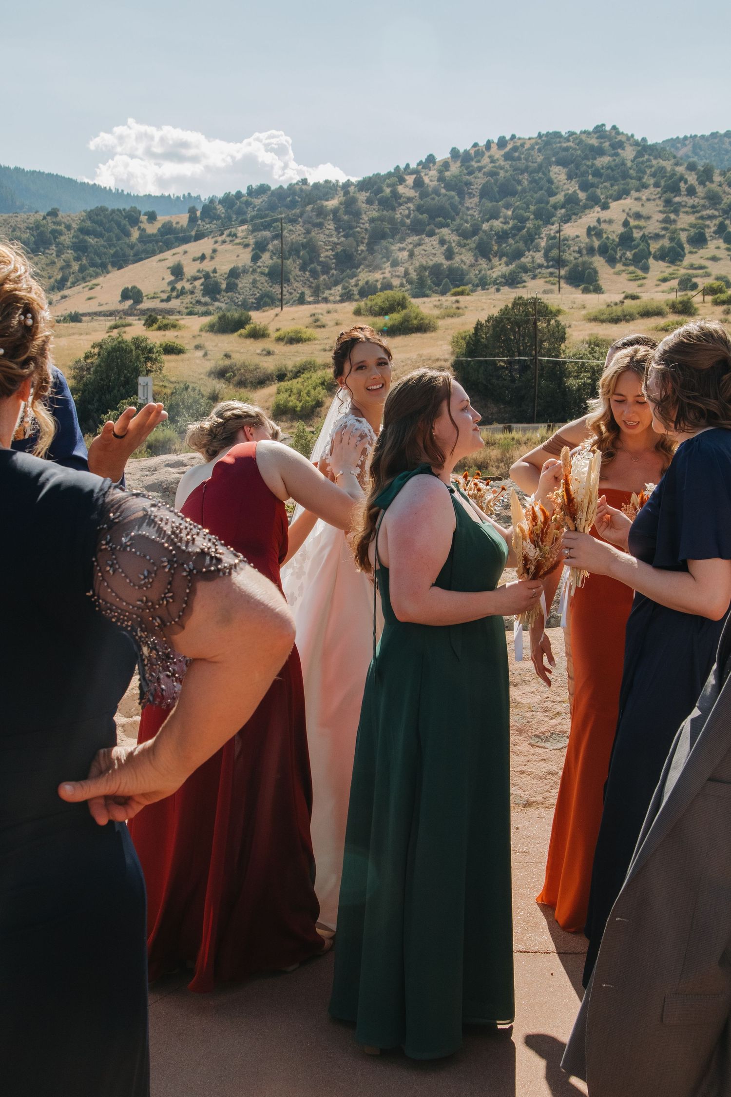 Wedding party in autumn-colored dresses celebrating against mountain landscape.