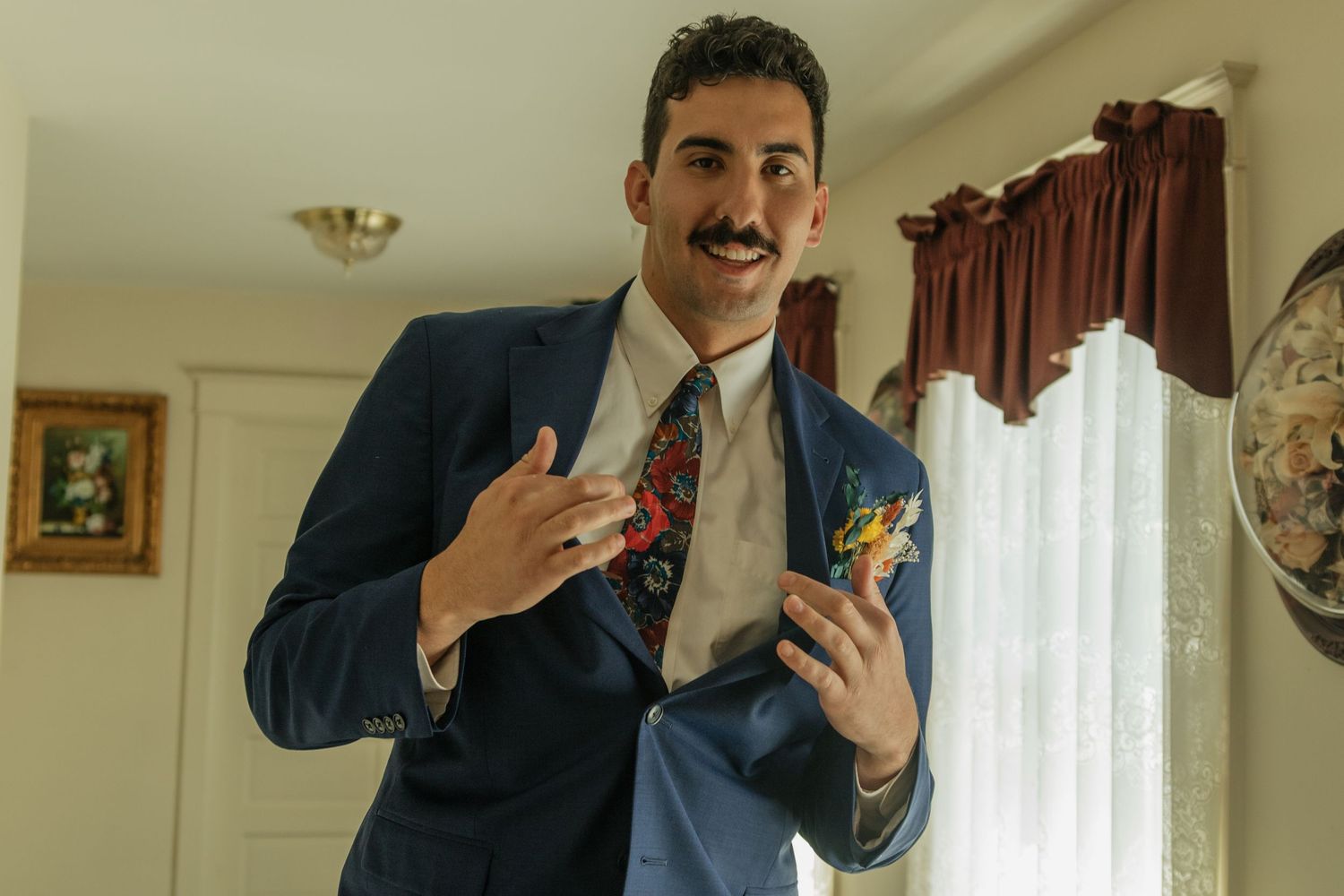 A person in a navy suit adjusts their boutonniere while preparing for a formal event.