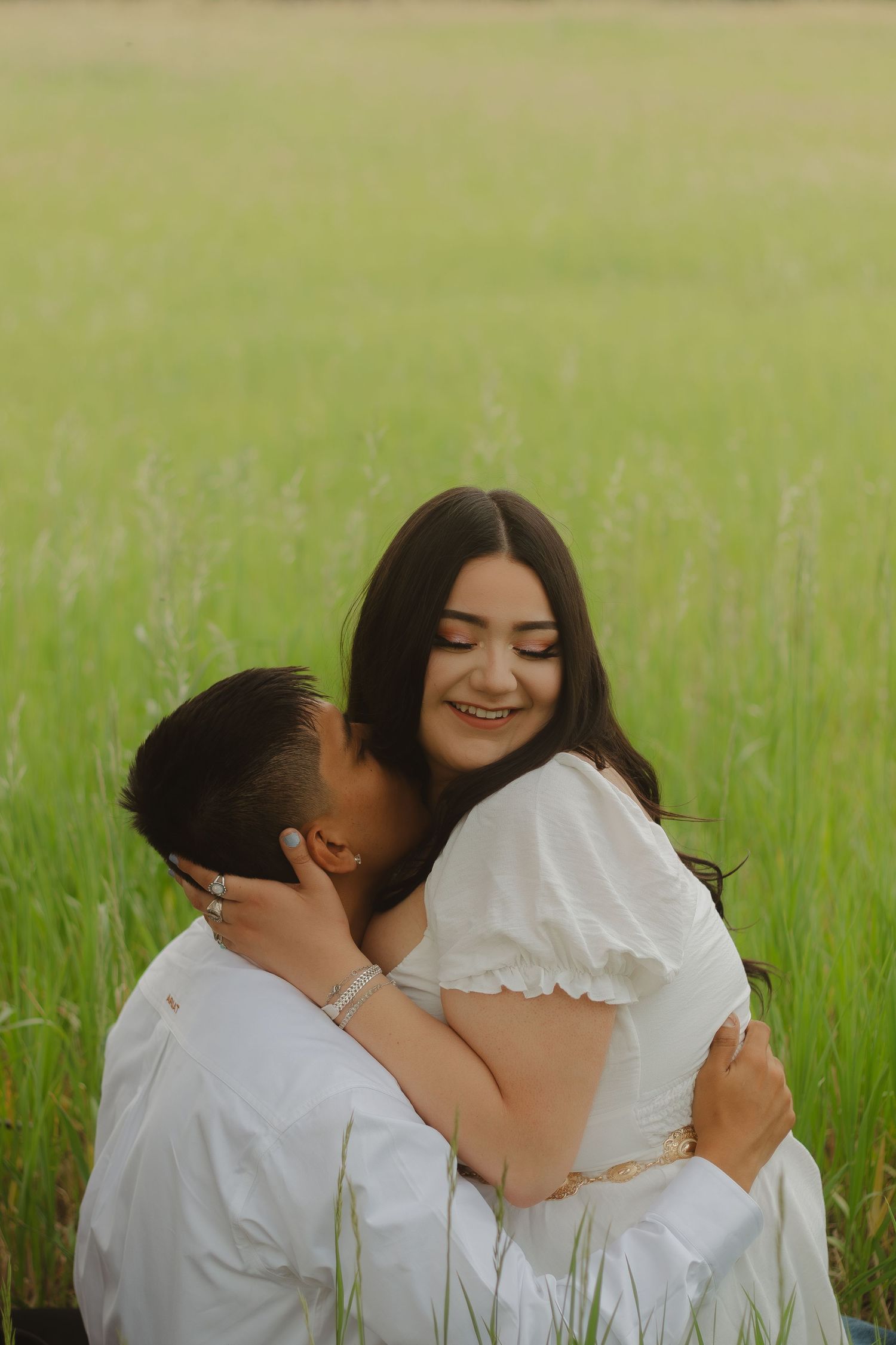 Couple in white clothing embracing and laughing together in a sunny meadow.
