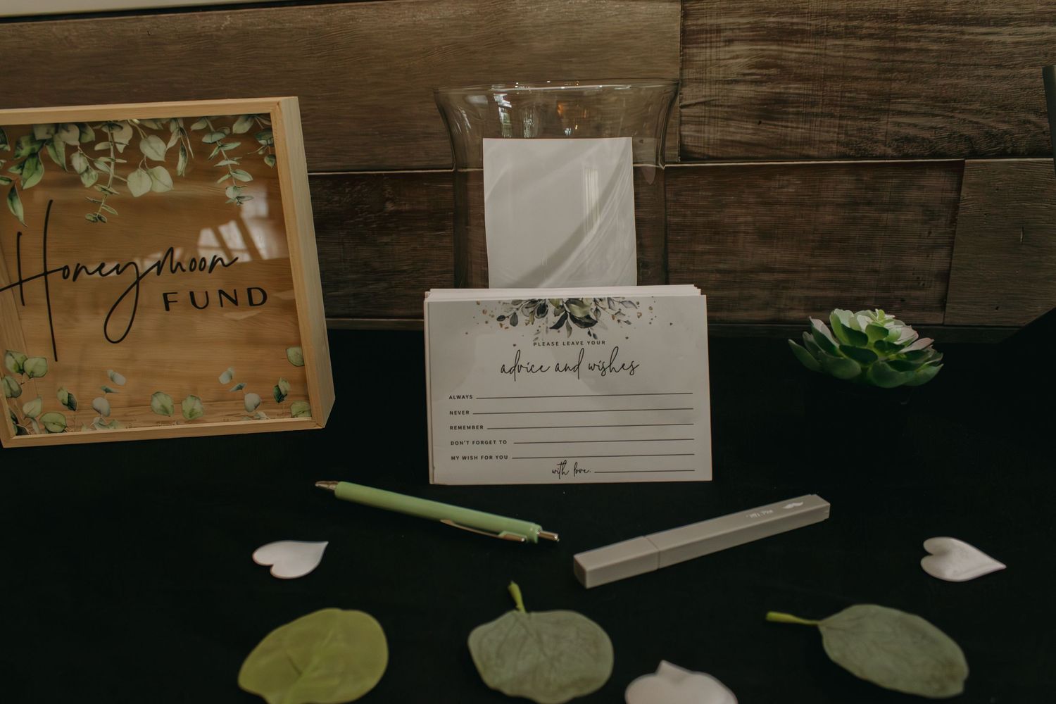 Rustic wooden table decorated with wedding cards and greenery.