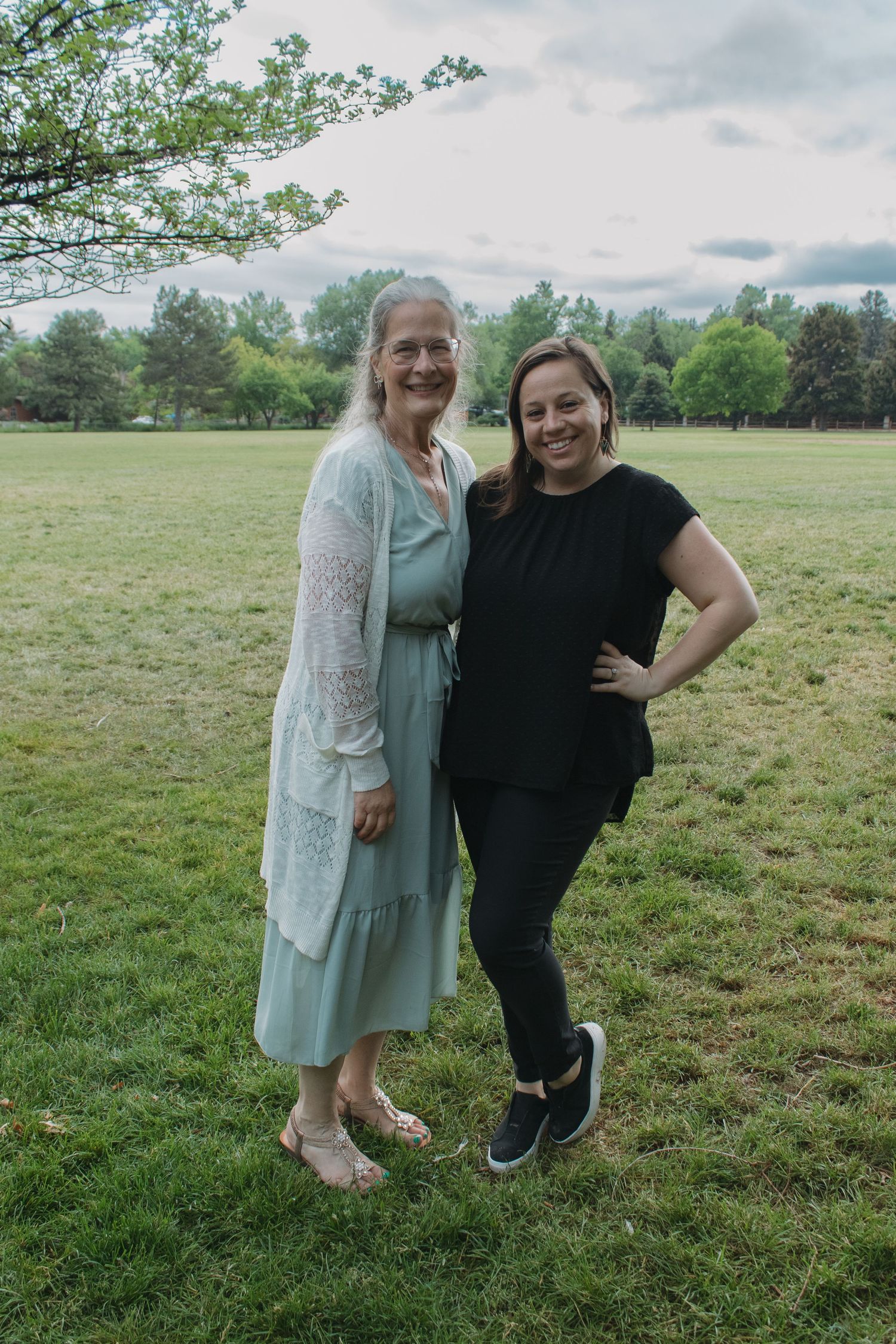 Two family members share a happy moment together on a grassy field during wedding celebrations.