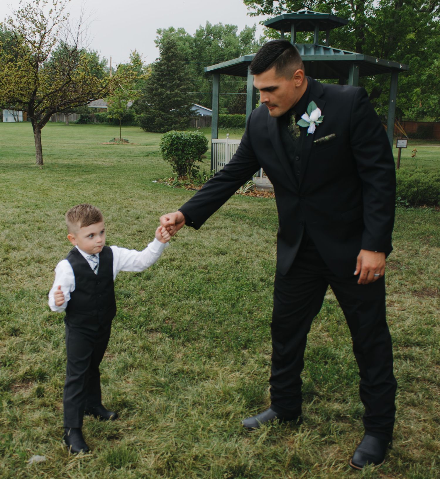 Ring bearer and wedding party member interact playfully on grassy outdoor setting.