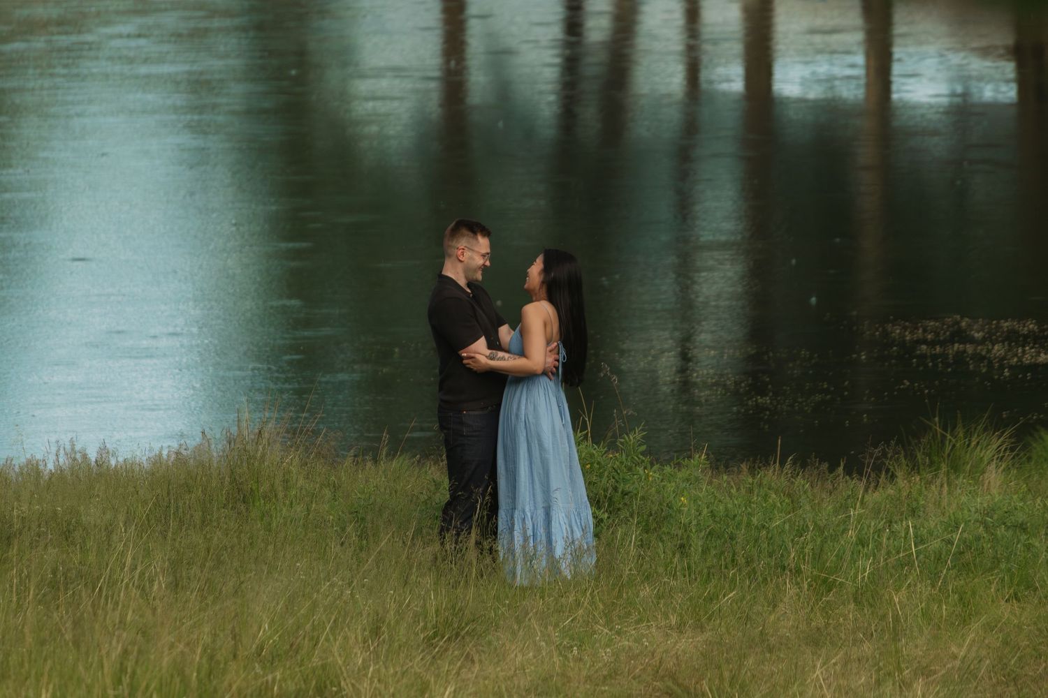 Intimate moment captured by the water with a light blue dress contrasting against dark clothing.
