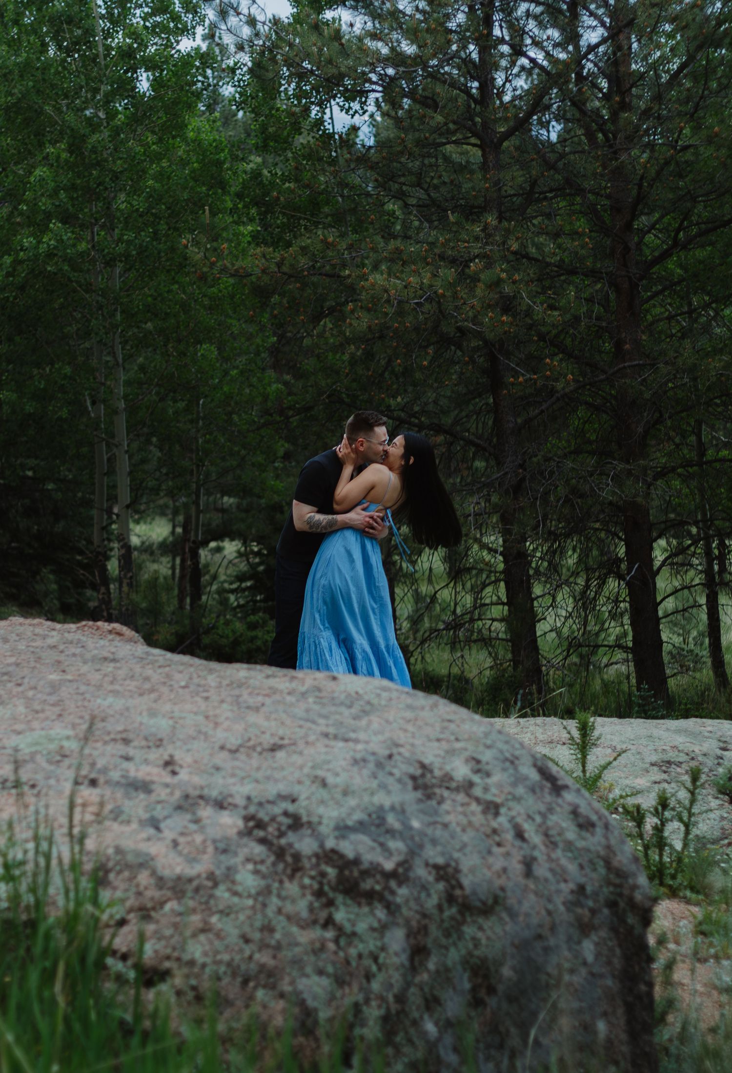 A romantic moment shared between a couple on a rocky outcrop in a pine forest.