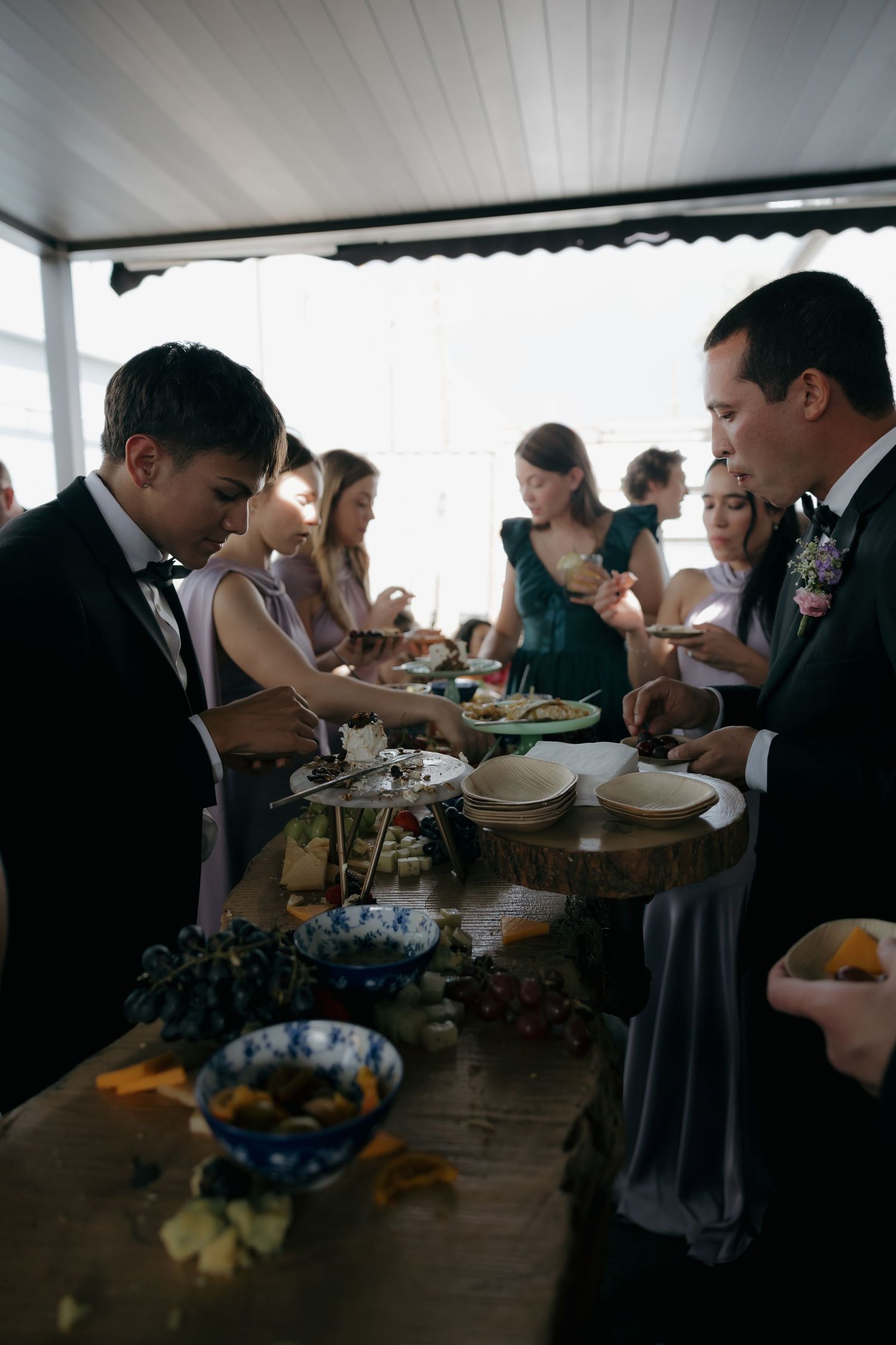 Wedding guests serve themselves at a rustic wooden buffet table decorated with grapes and flowers during reception.