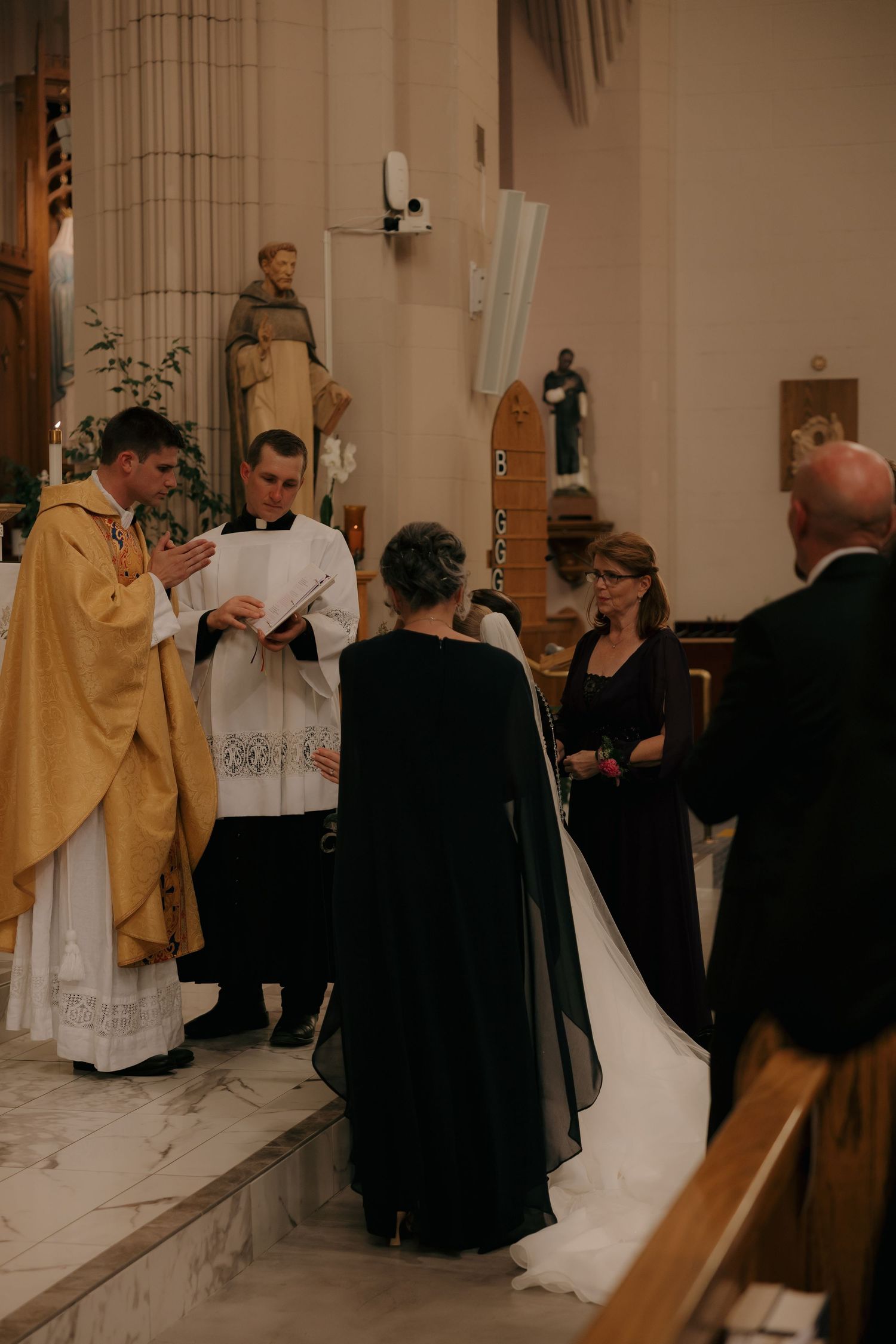 Catholic wedding ceremony with priest in gold vestments reading vows to couple at church altar.