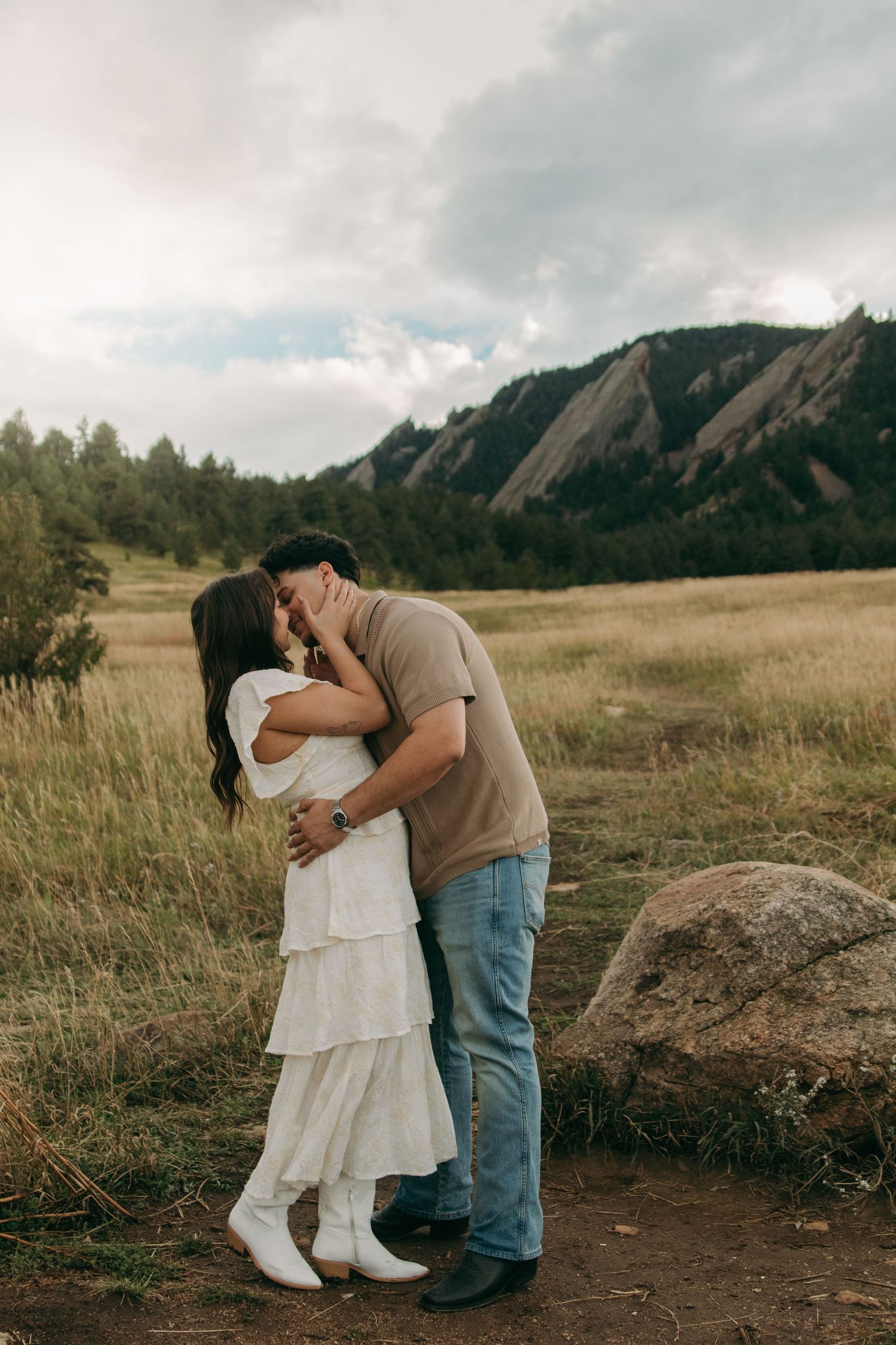 Couple kissing in open meadow with dramatic Flatirons rock formation in background.