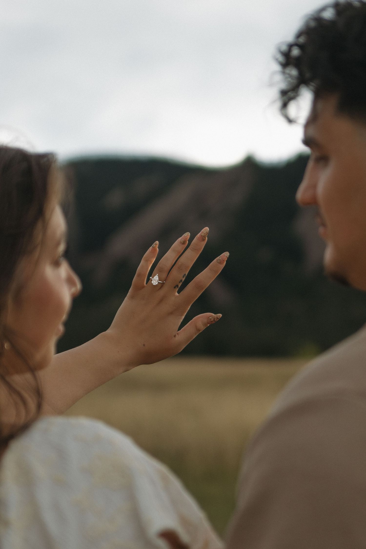 Woman displaying diamond engagement ring with rocky mountain landscape in background.