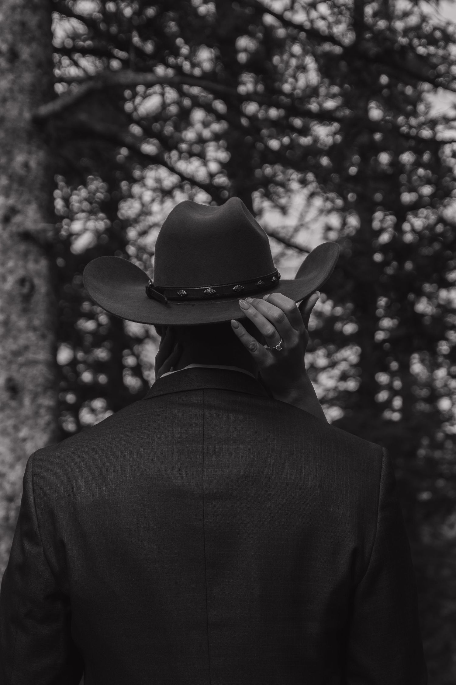 Back view of someone wearing a black cowboy hat and suit jacket in a forest.