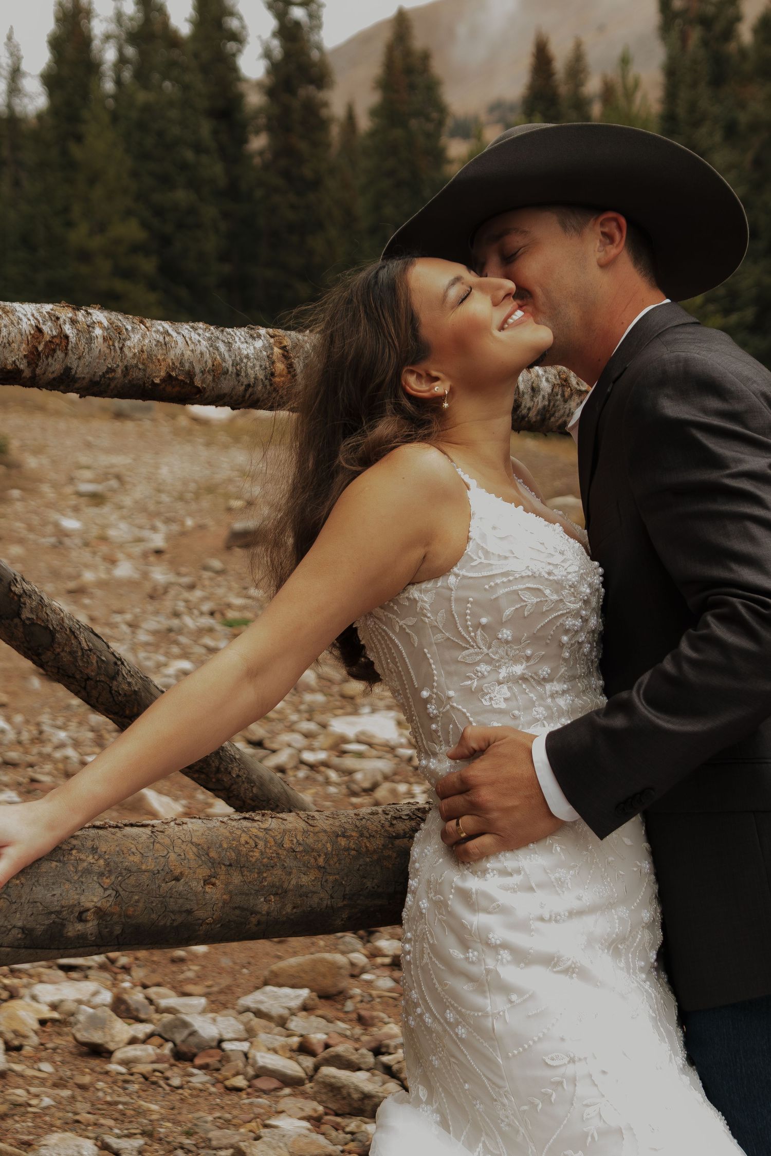 A romantic embrace captured against a mountain backdrop with evergreen trees.