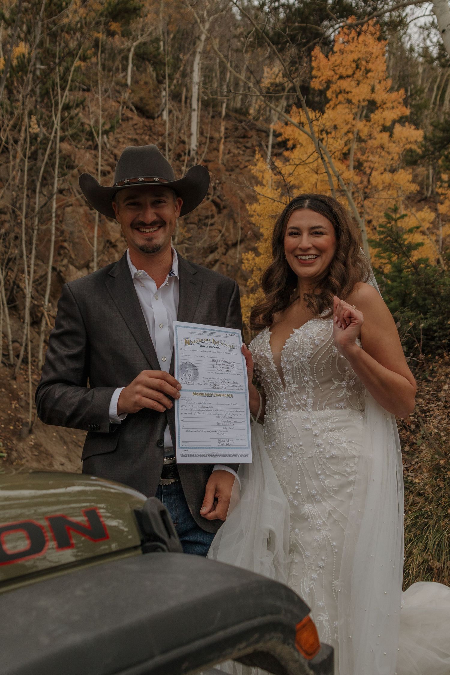 Couple displays their marriage certificate against a backdrop of autumn trees.