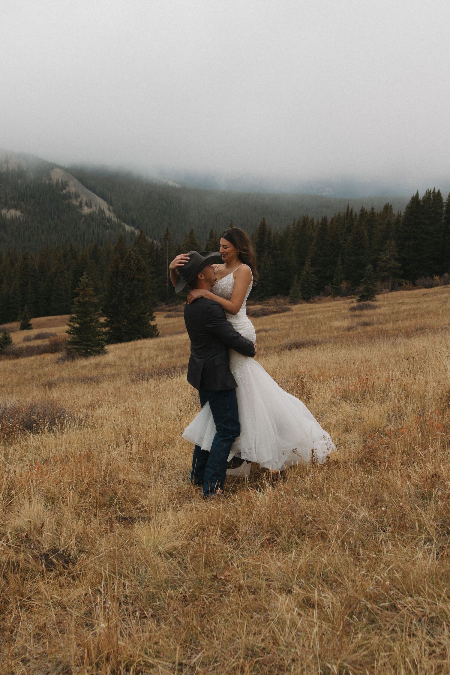 Couple dancing together in a scenic mountain meadow with evergreen trees in the background.
