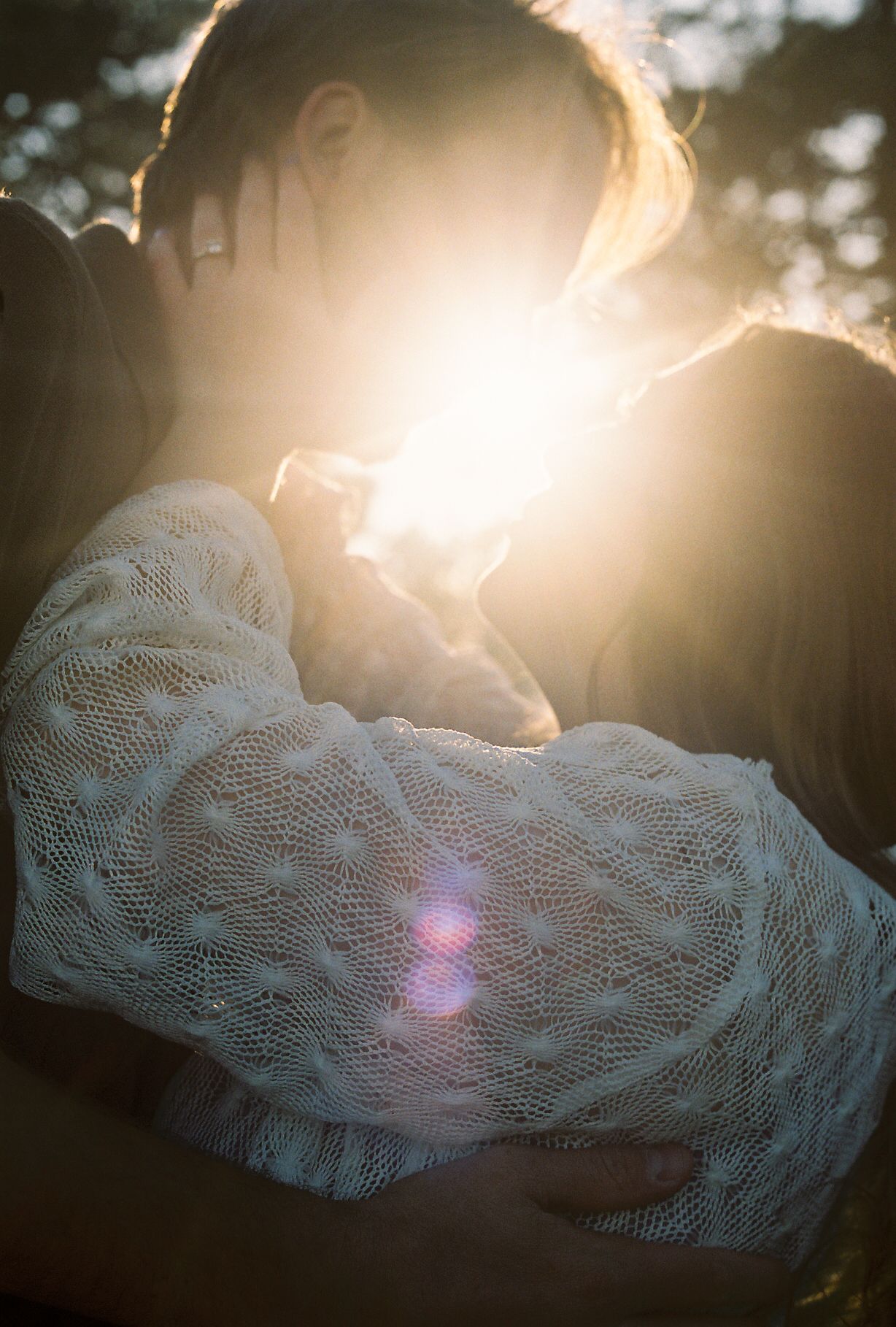 Couple embracing with golden sun flare glowing between them outdoors.