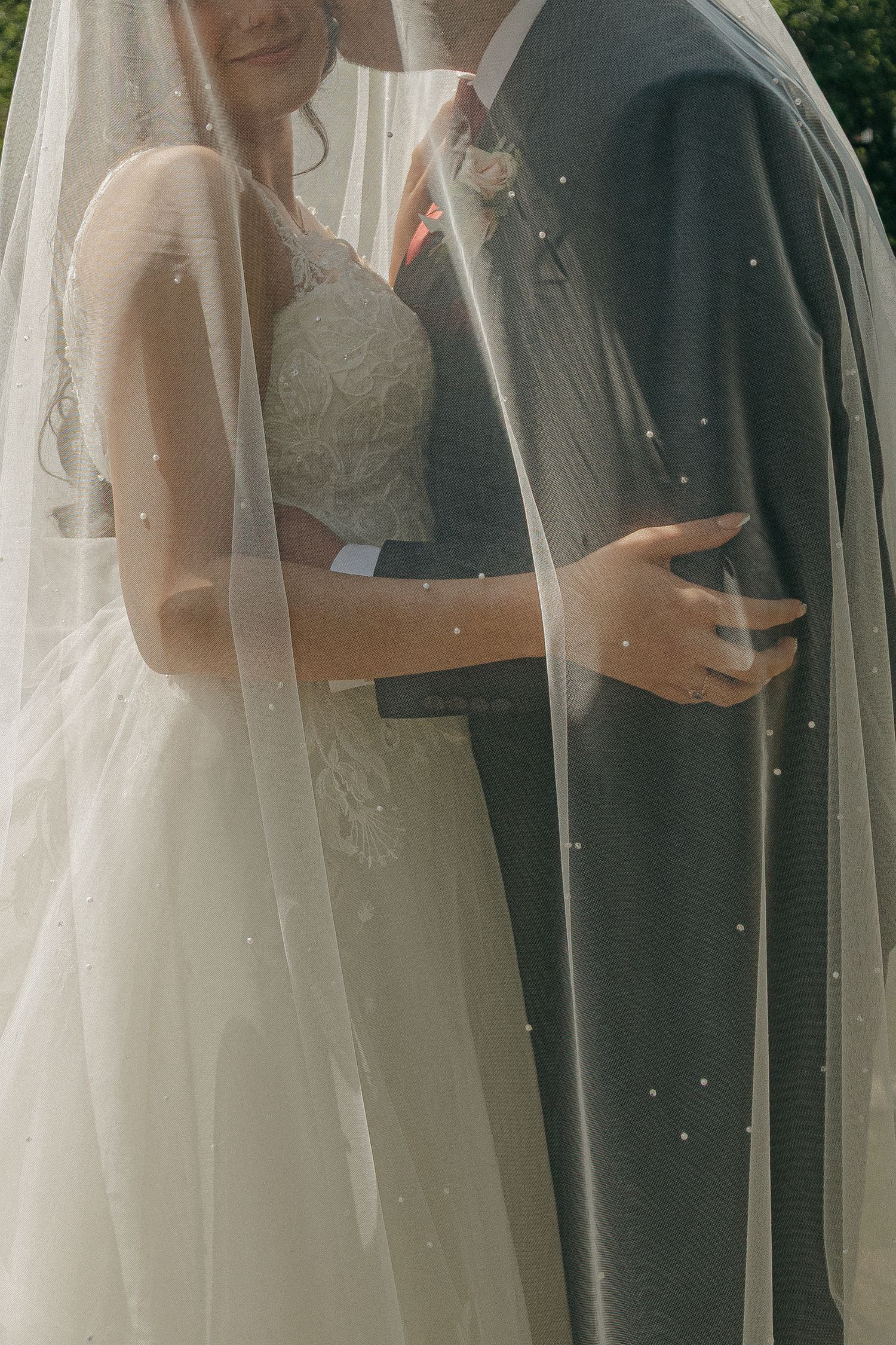 Close-up of bride and groom embracing under a delicate pearl-dotted wedding veil.