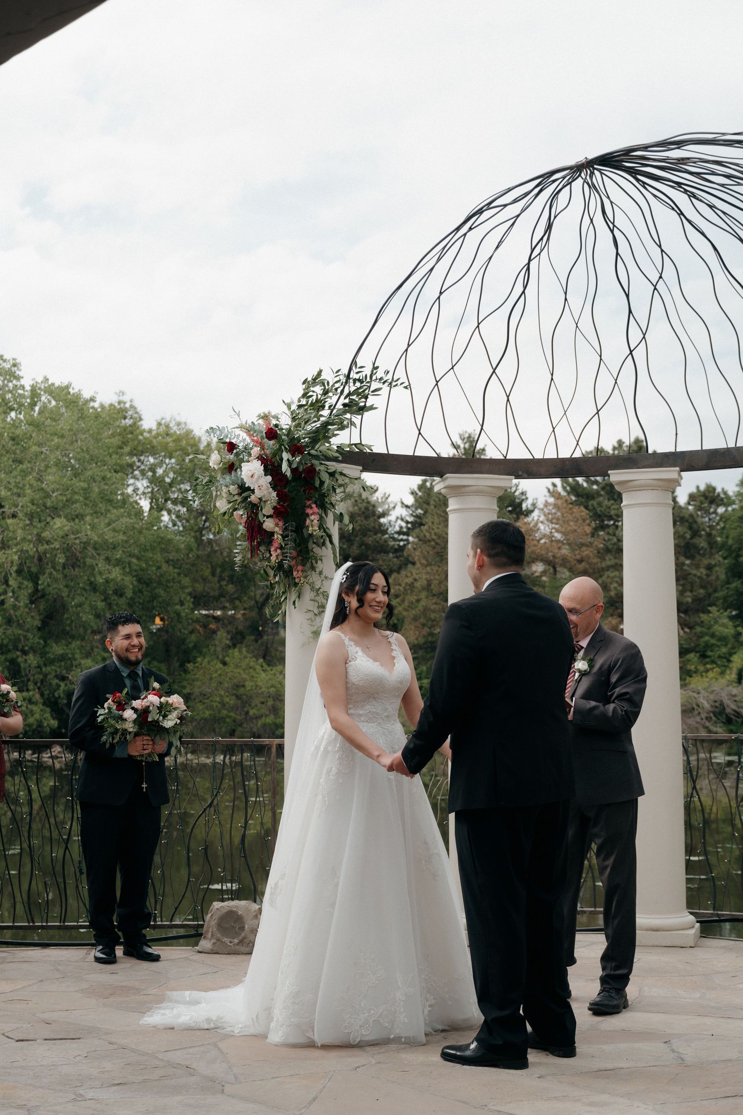 Bride and groom exchange vows at outdoor altar with floral arch and white columns at wedding.