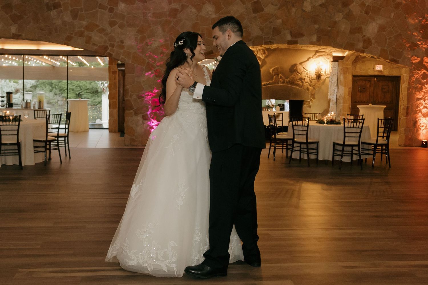 Bride and groom share intimate first dance in warmly lit rustic wedding reception venue.