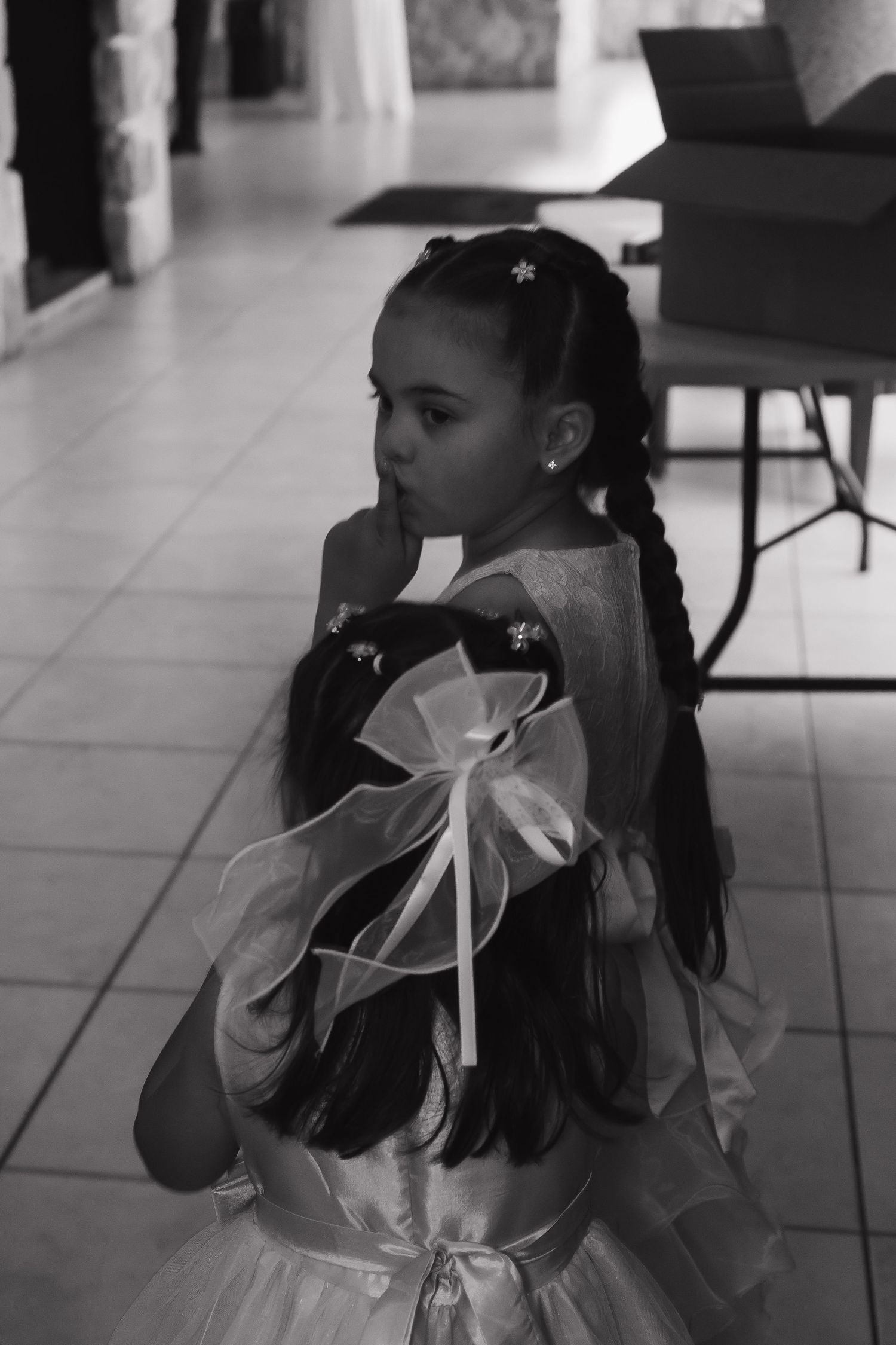 Young girl in elegant white dress with ribbon bow and braided hair at a formal event.