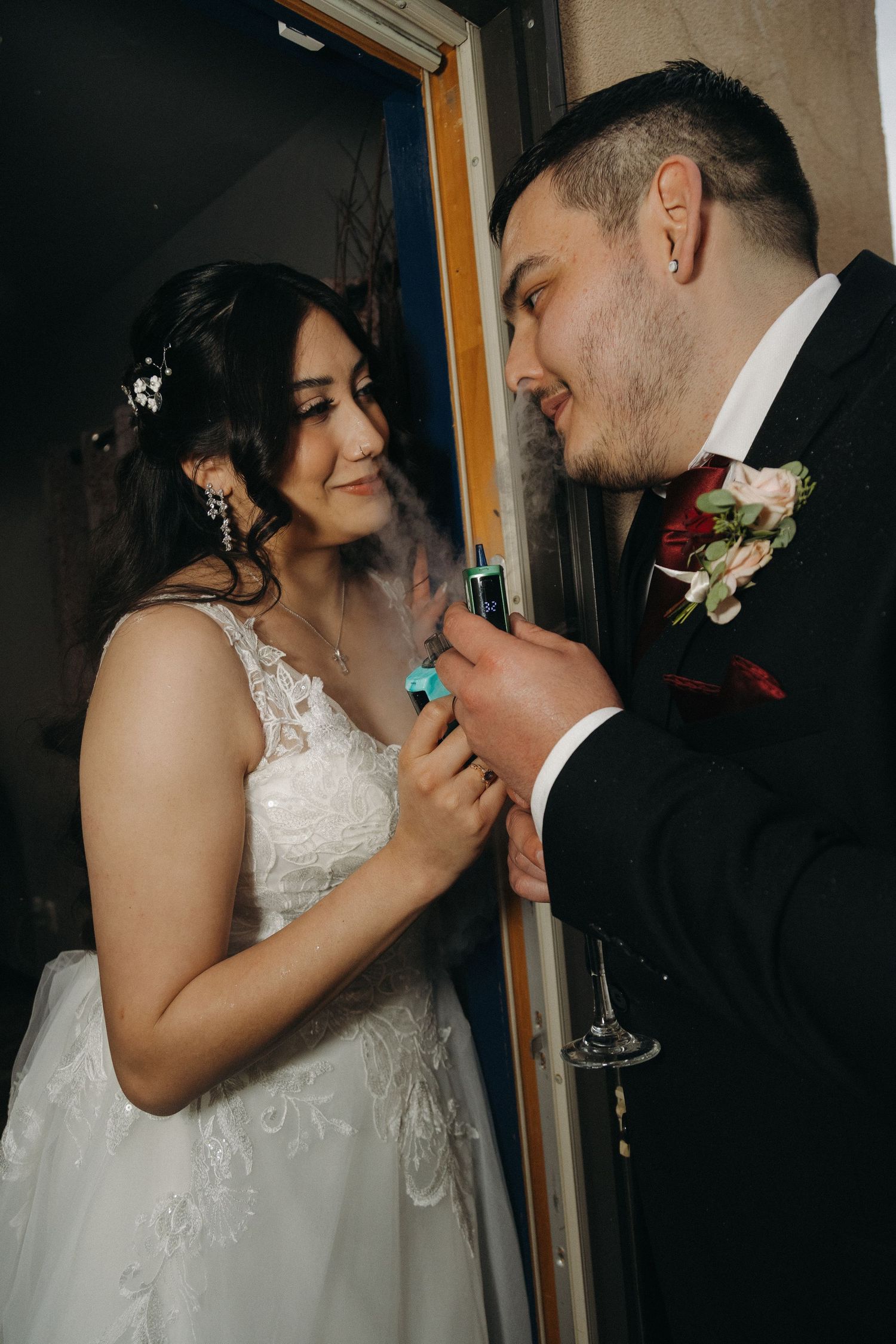 Bride and groom sharing a playful moment with a vape, smiling together in their wedding attire.