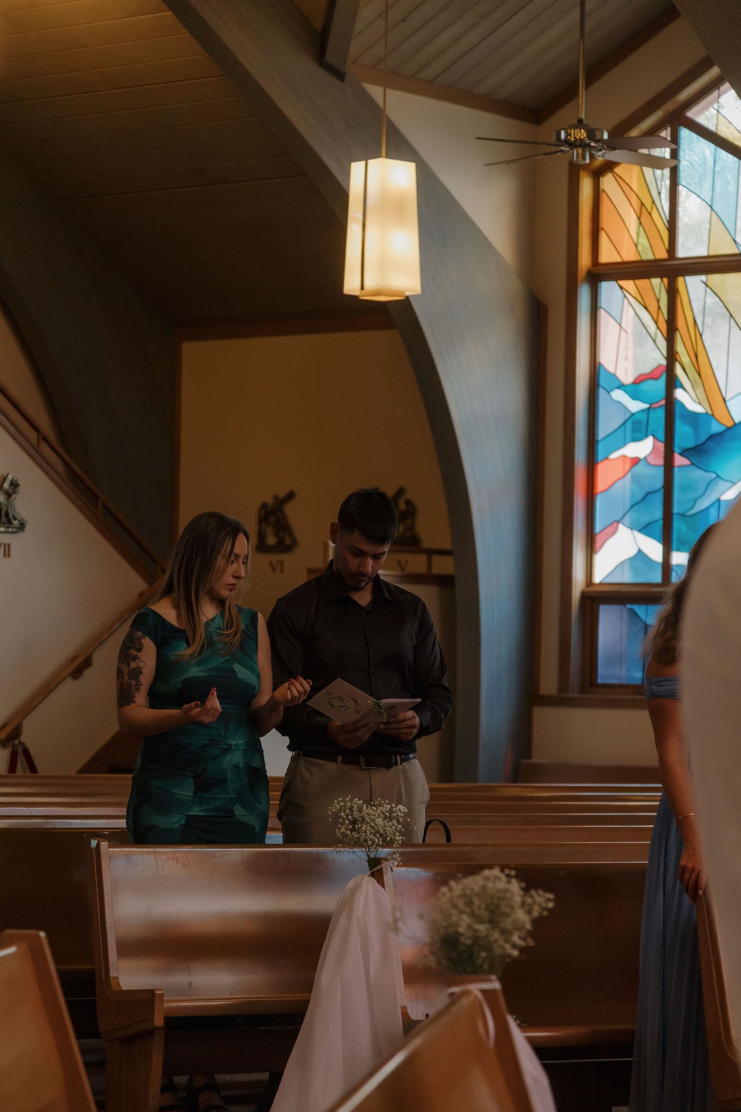 Couple reading from a book together inside a dimly lit church with stained glass window nearby.