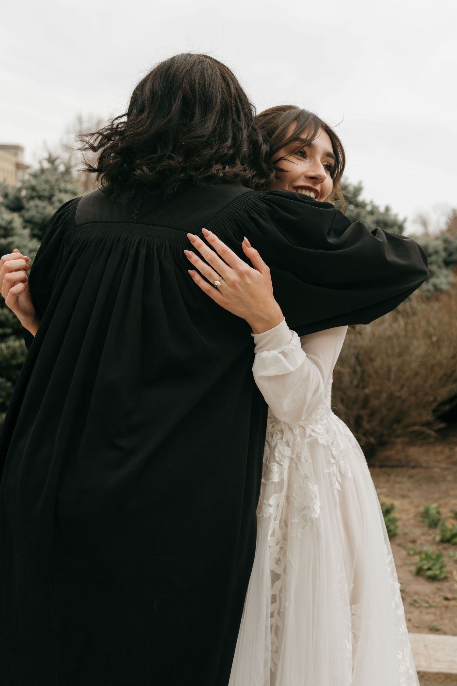 A couple embraces in an intimate moment wearing black and white wedding attire outdoors.