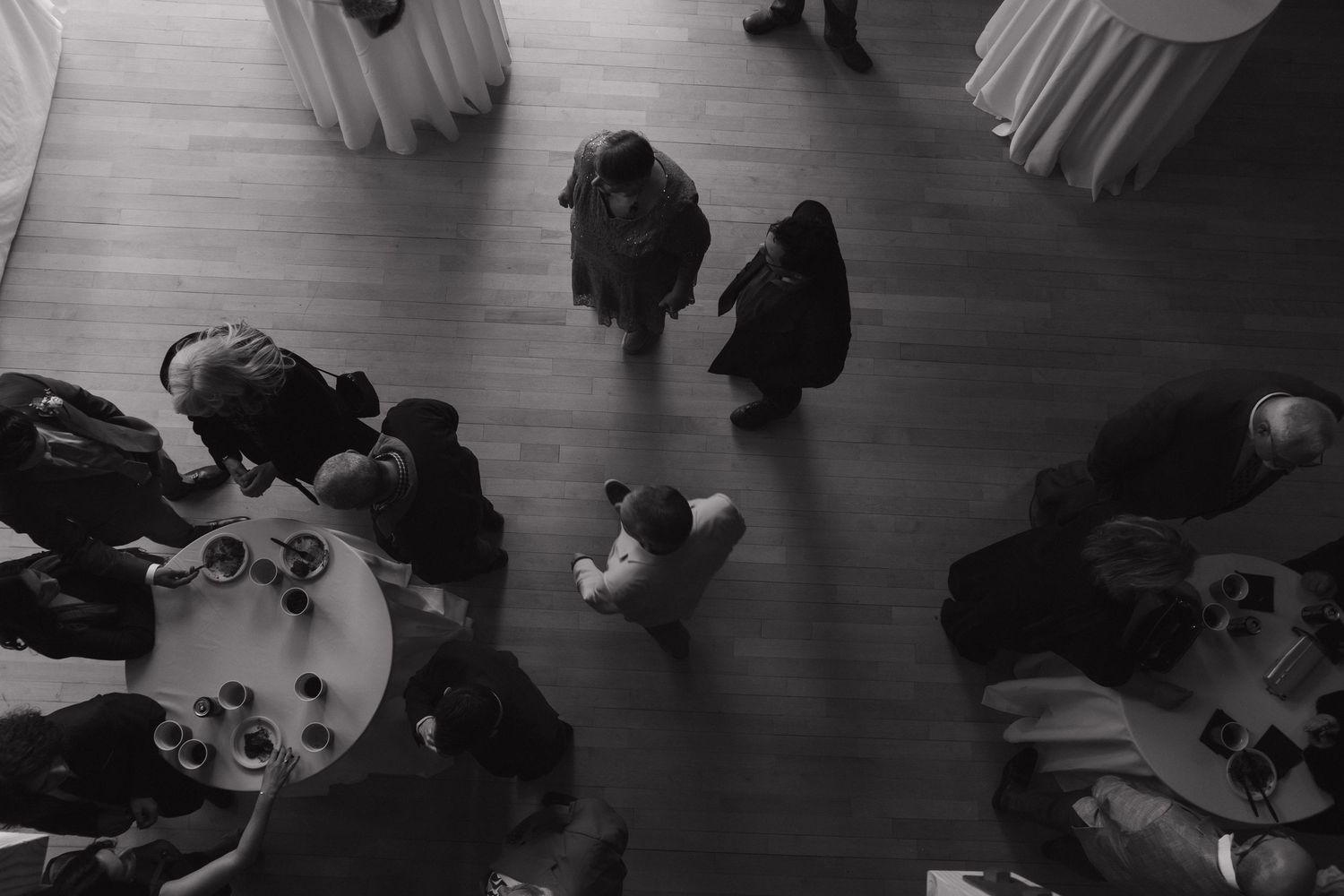 A black and white photo shows people dancing in a large ballroom with a polished floor.