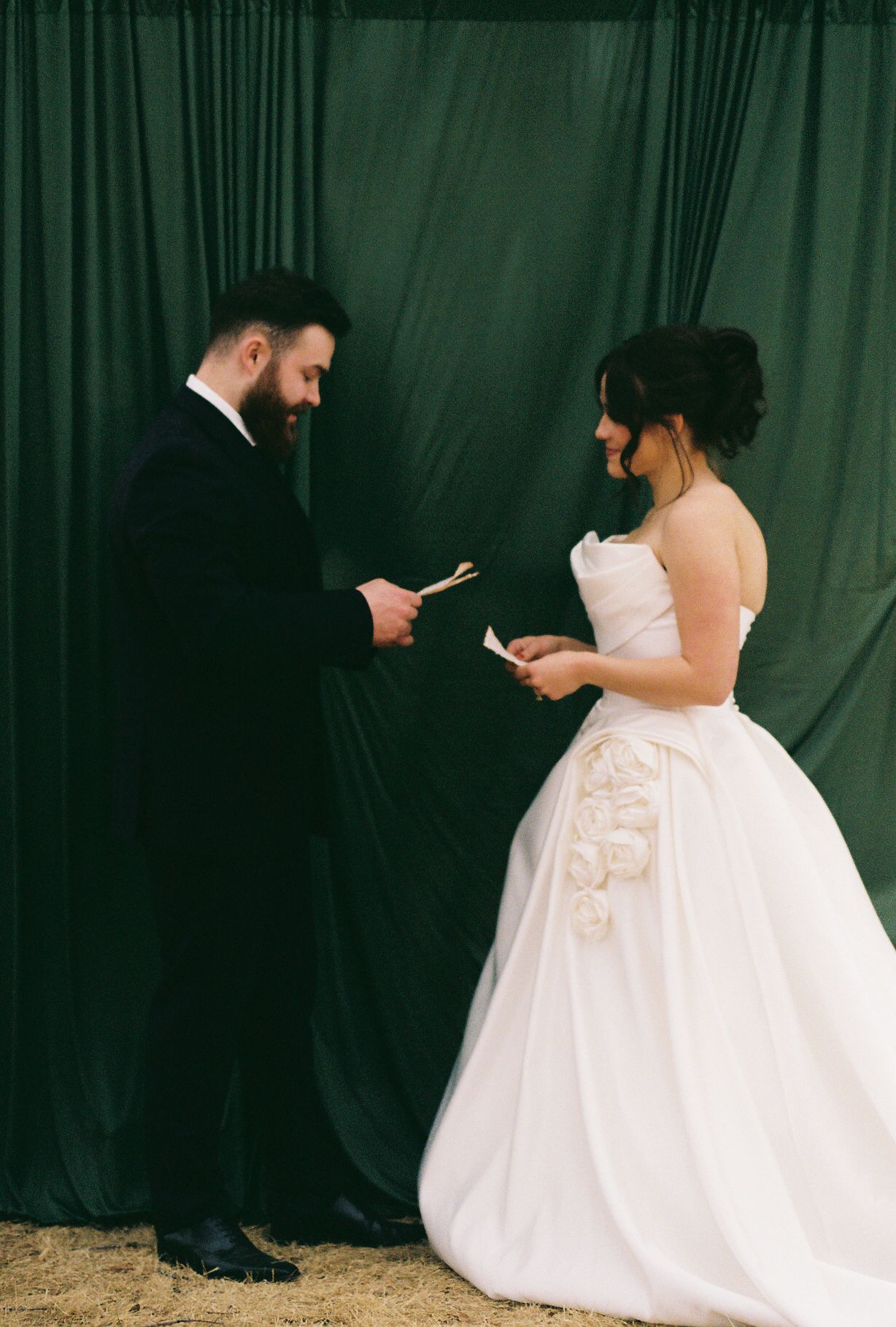 Wedding couple poses against dark backdrop with elegant white gown details.