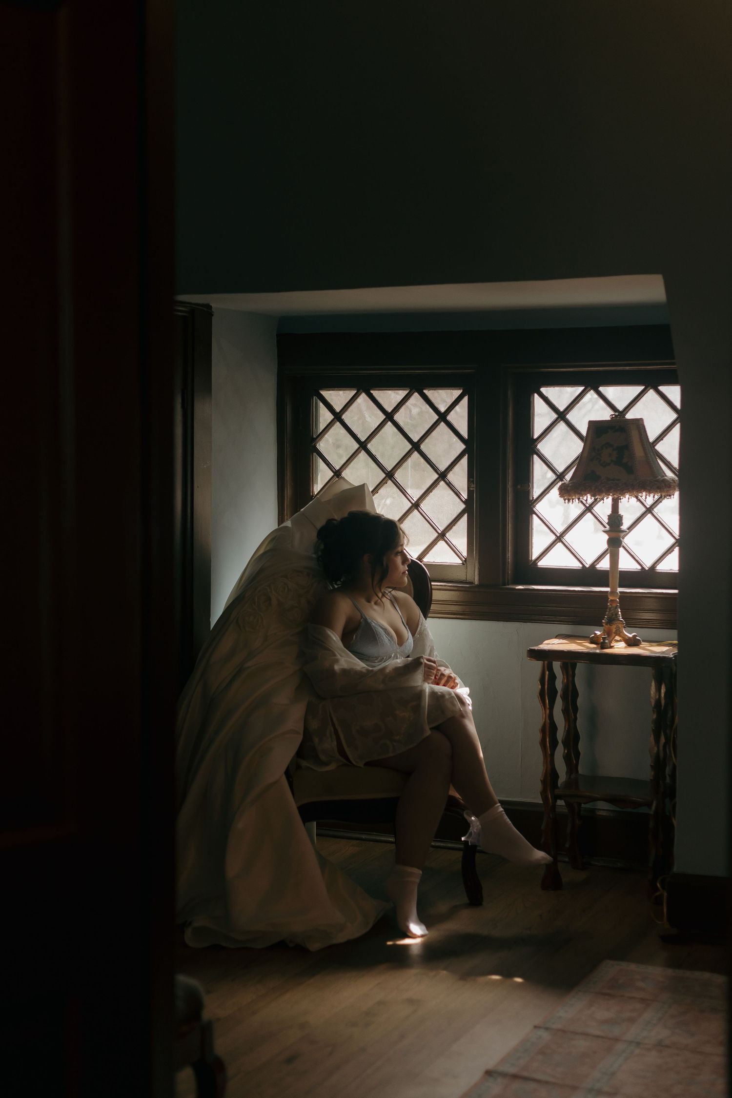 A silhouette of someone in a wedding dress sitting by a window with lattice pattern.