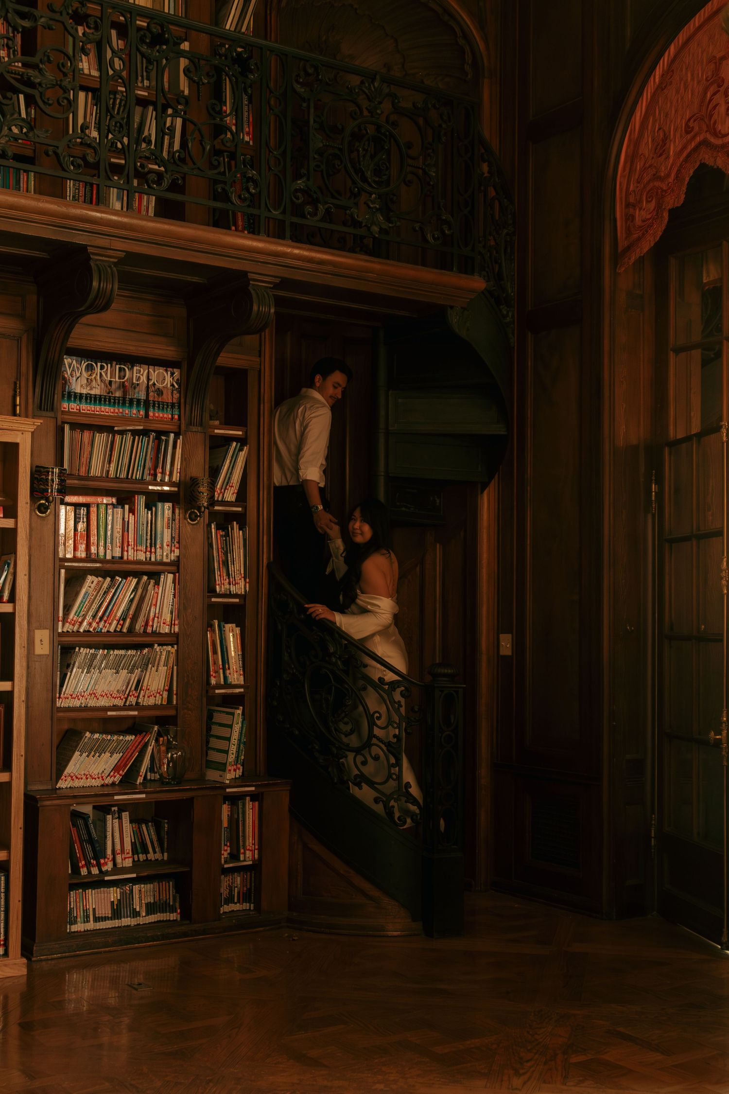 A couple dances intimately in a dimly lit library with wooden bookshelves lining the walls.