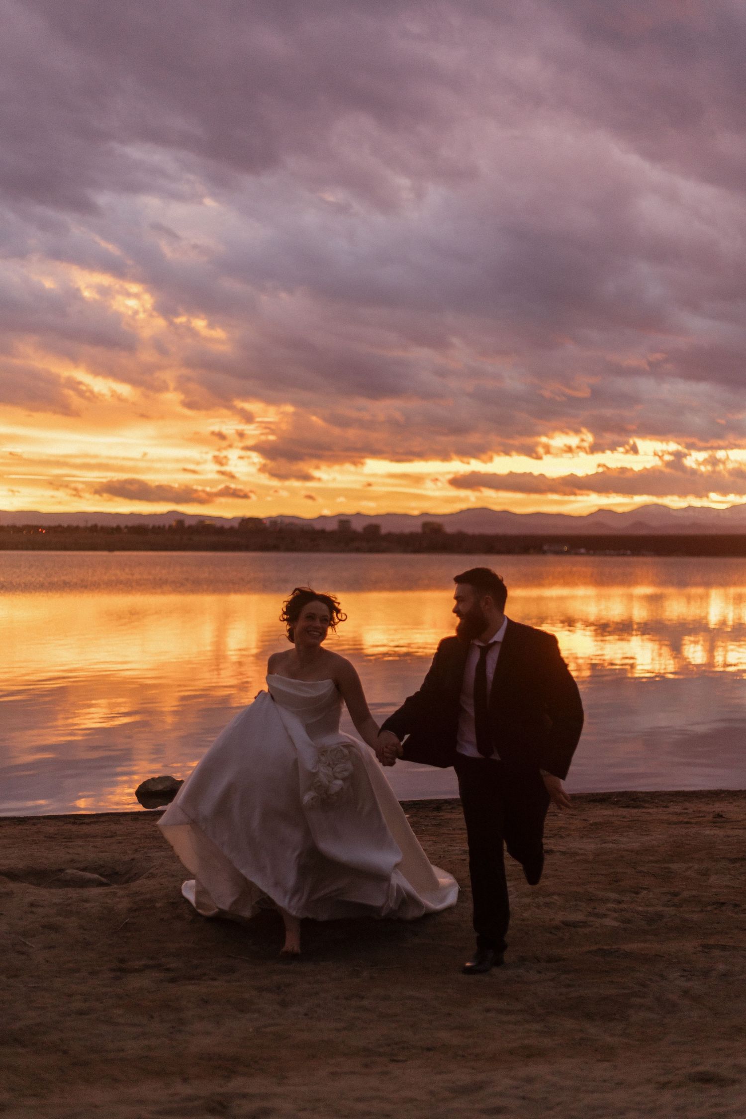 Silhouettes of a couple walking on beach during dramatic orange and purple sunset.