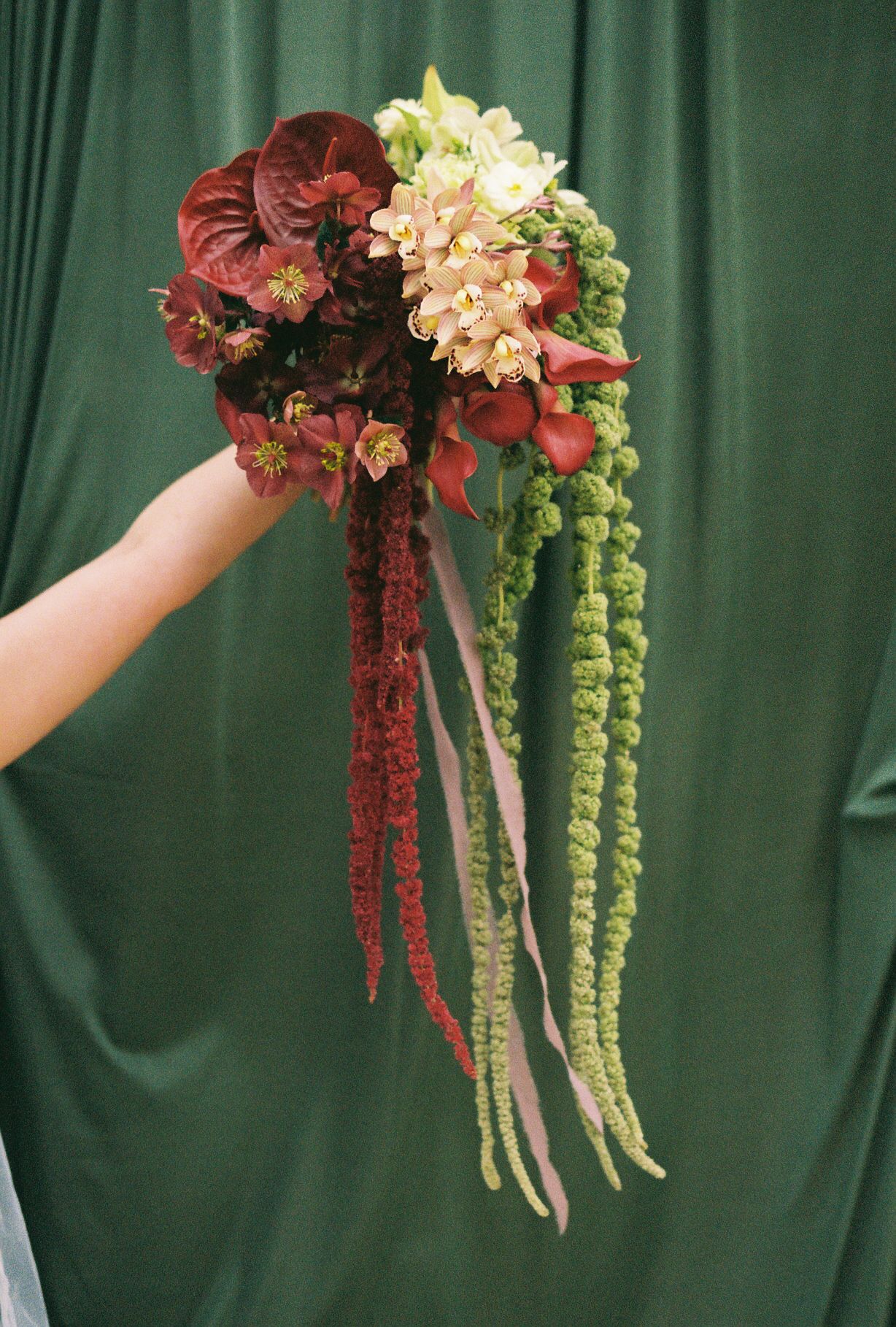 Elegant wedding bouquet with cascading red and cream flowers against a green backdrop.